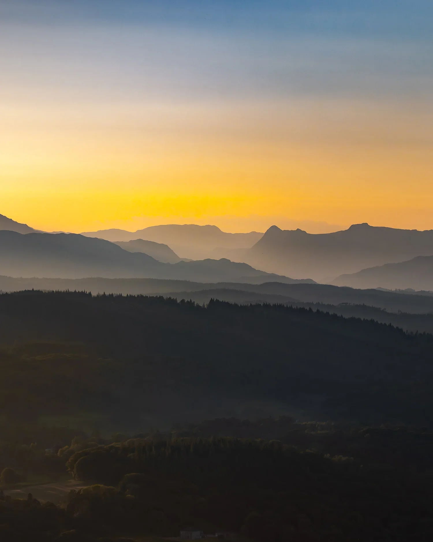Sunset over multiple mountain ranges with a colorful sky and misty valleys.