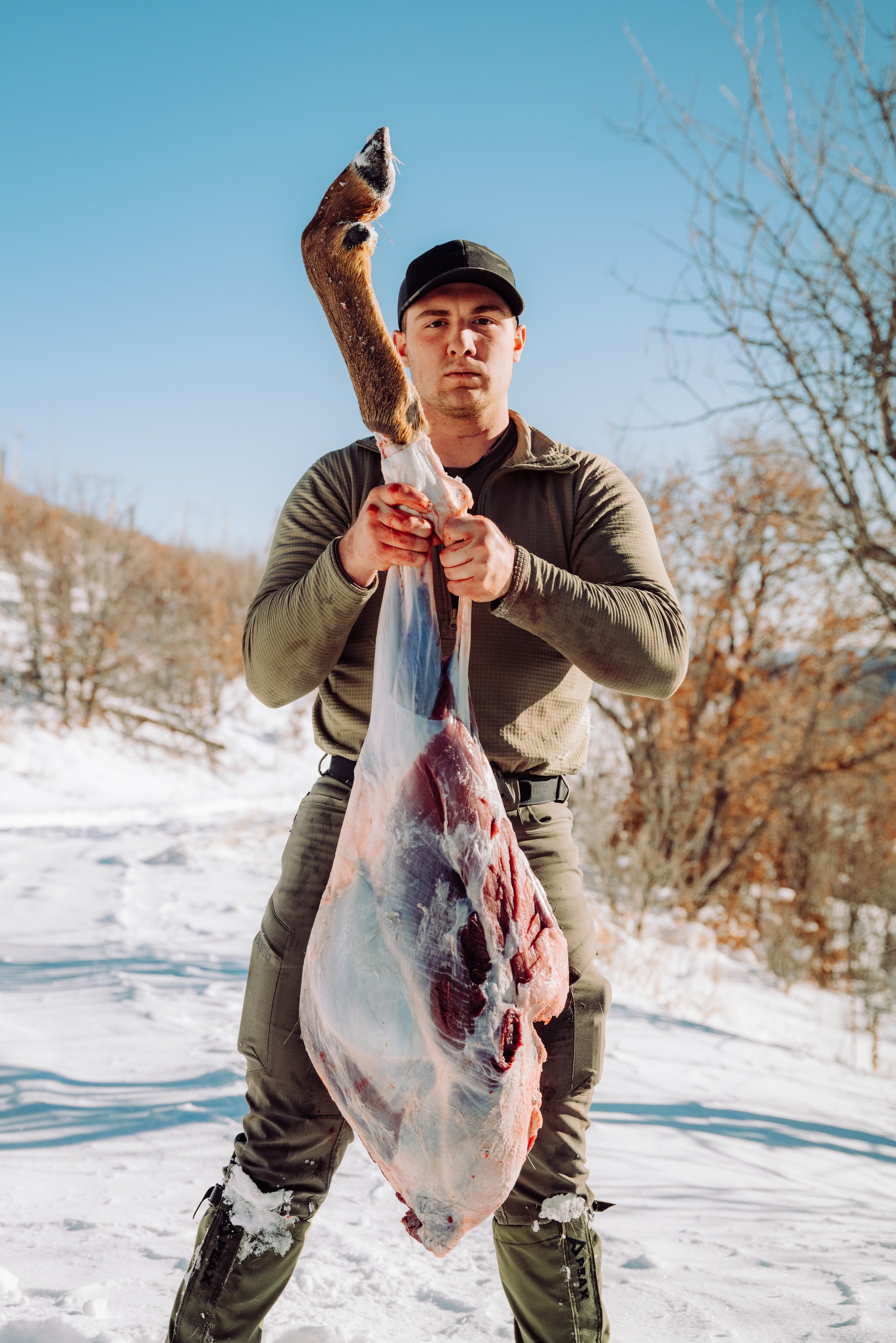 Man holding a large fish outdoors in a snowy landscape.