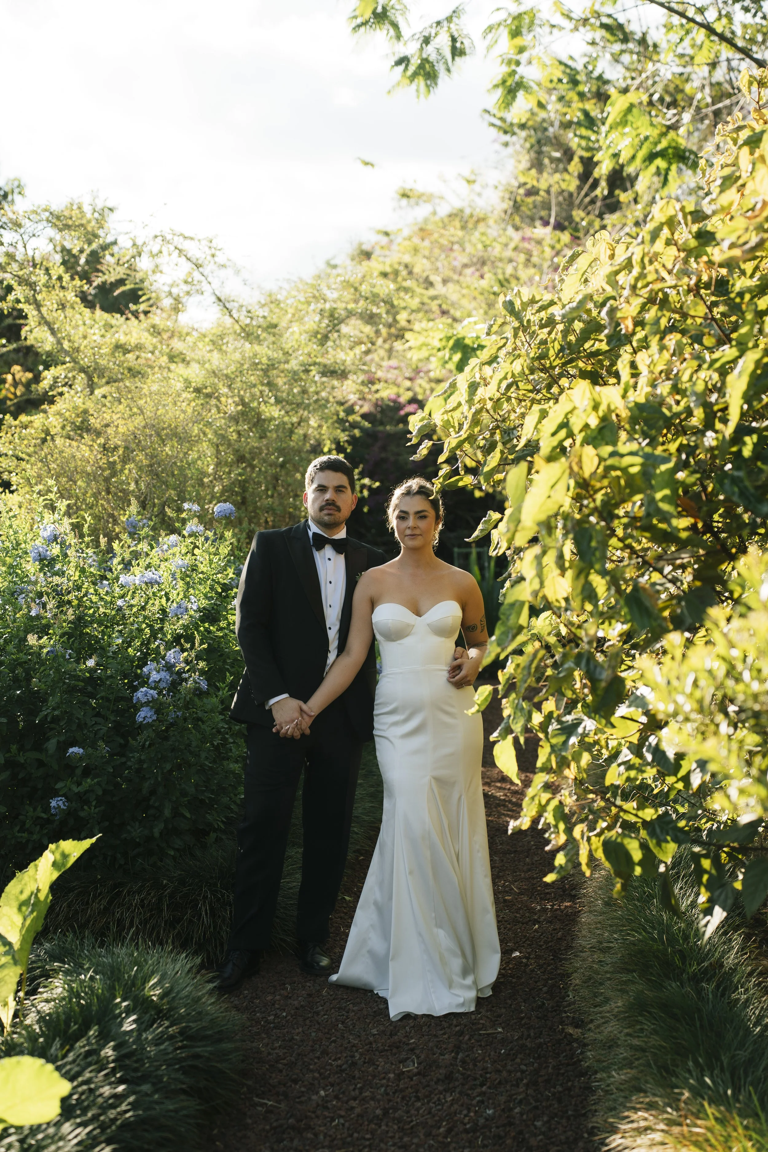 Novios recién casados tomados de la mano en un sendero rodeado de follaje y flores durante su boda en Costa Rica.