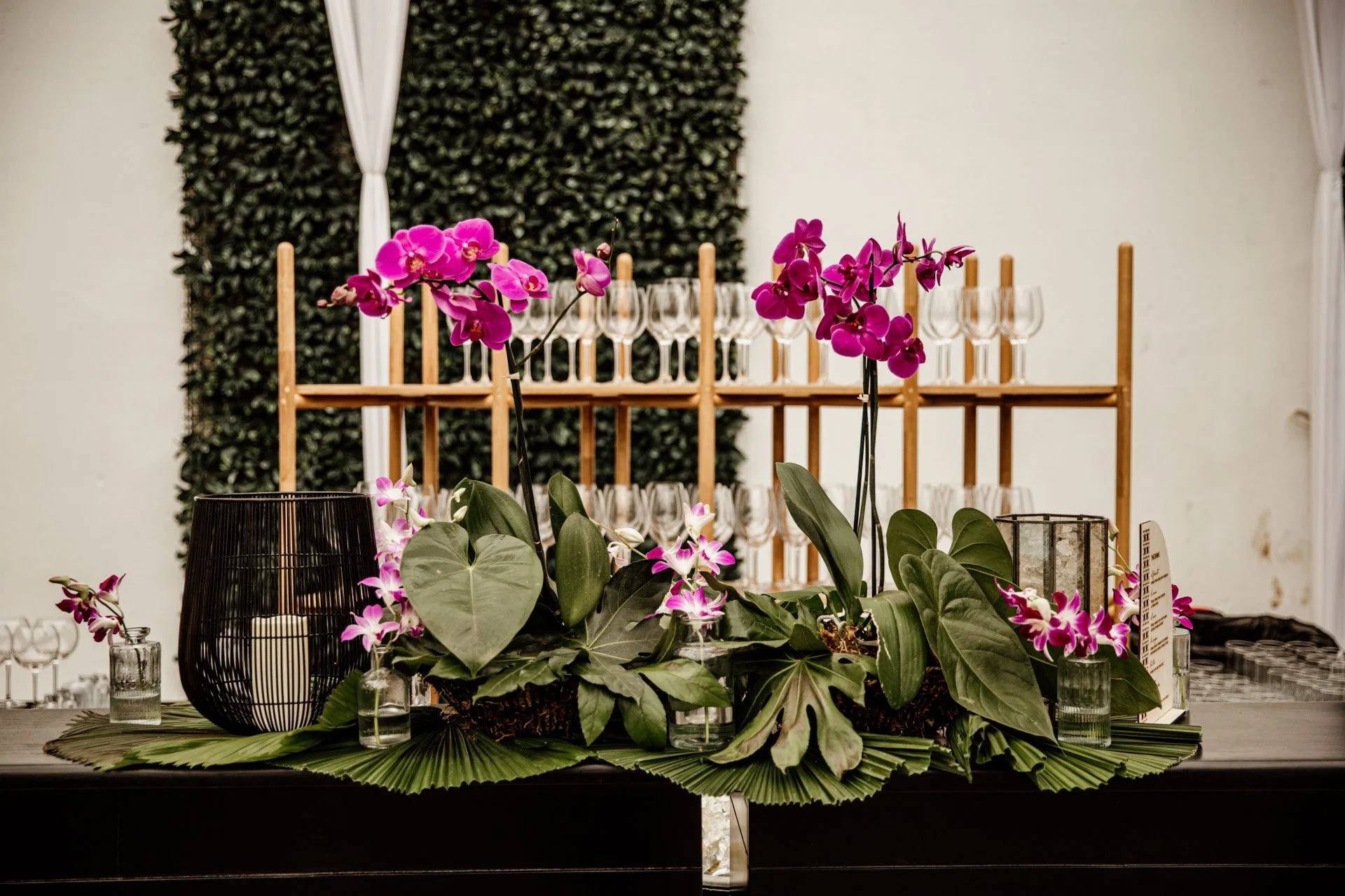 Detalle floral con orquídeas rosadas, hojas decorativas y velas sobre una mesa ambientada para una boda en Costa Rica.