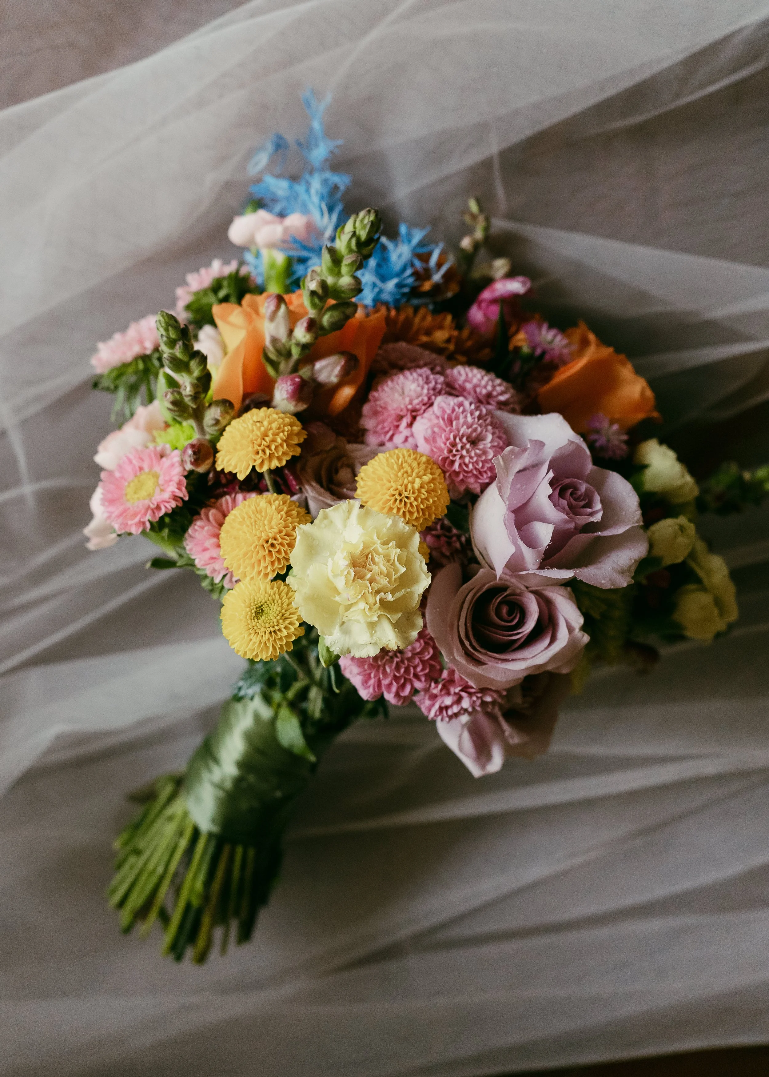 A bouquet of various colorful flowers including roses, carnations, and other small blossoms wrapped with green ribbon.