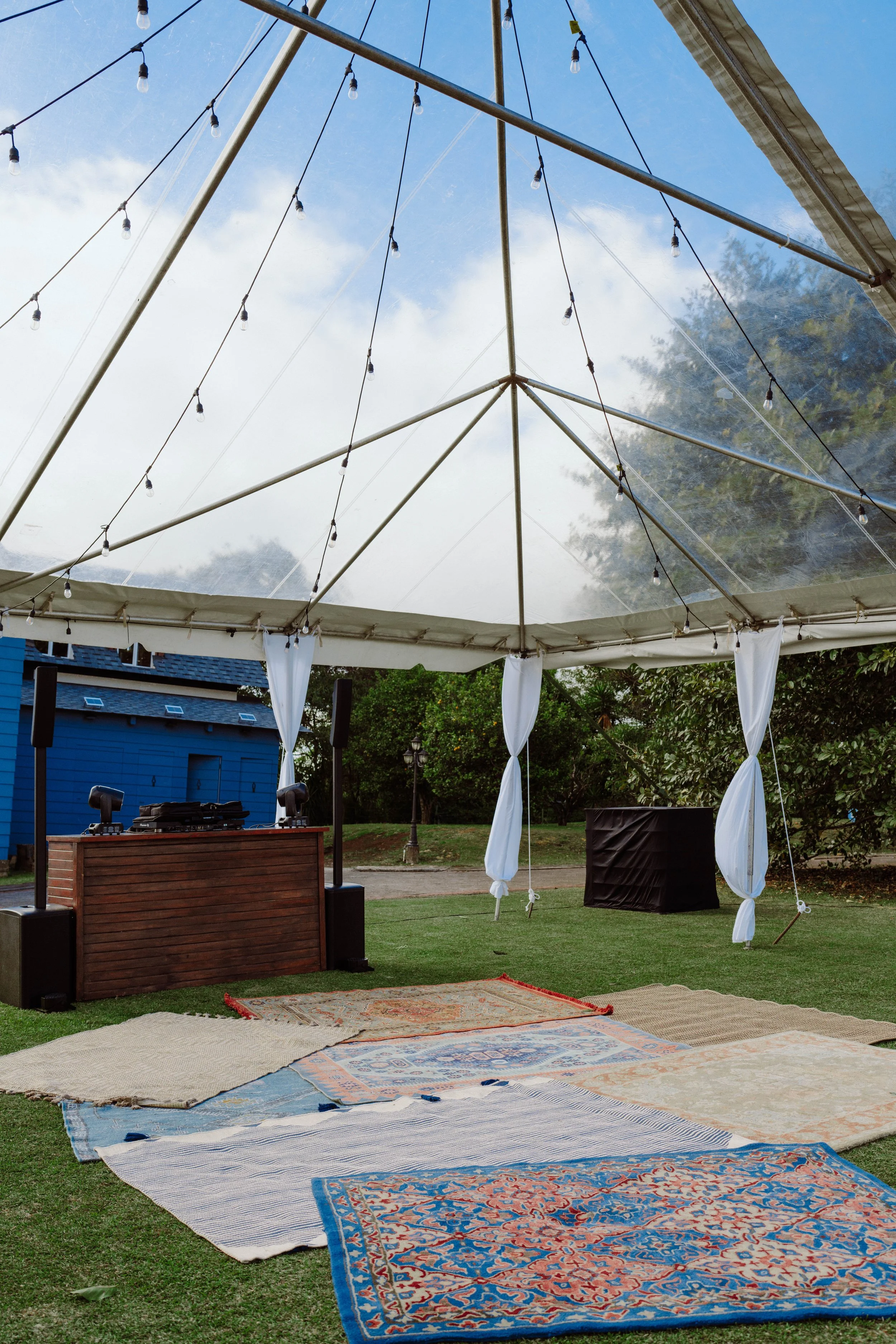 Espacio de fiesta al aire libre con carpa transparente, alfombras sobre el césped y cabina de DJ preparada para una boda en Costa Rica.