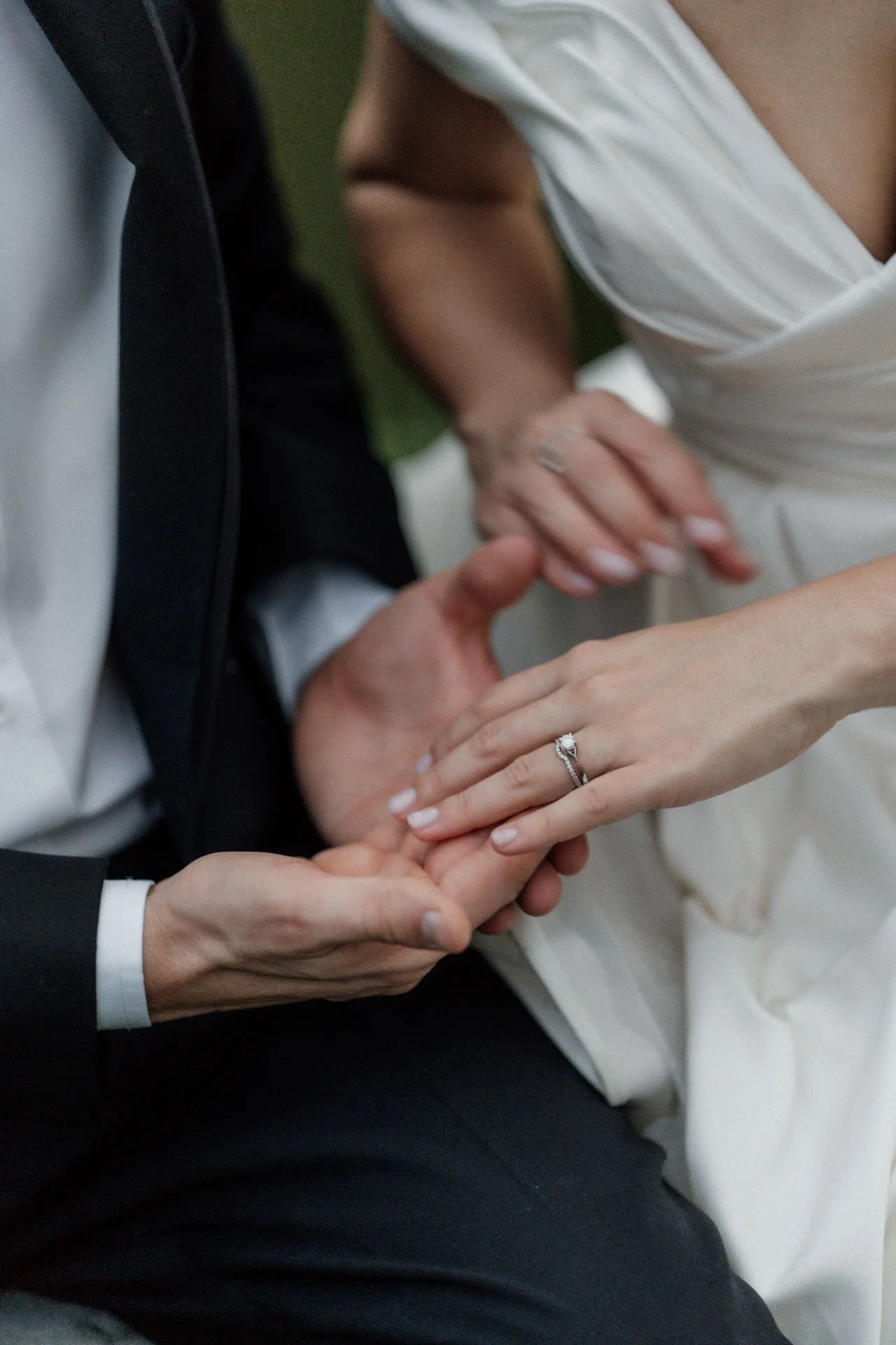 Close-up of a couple exchanging wedding rings, with their hands intertwined and the bride wearing a diamond engagement ring.
