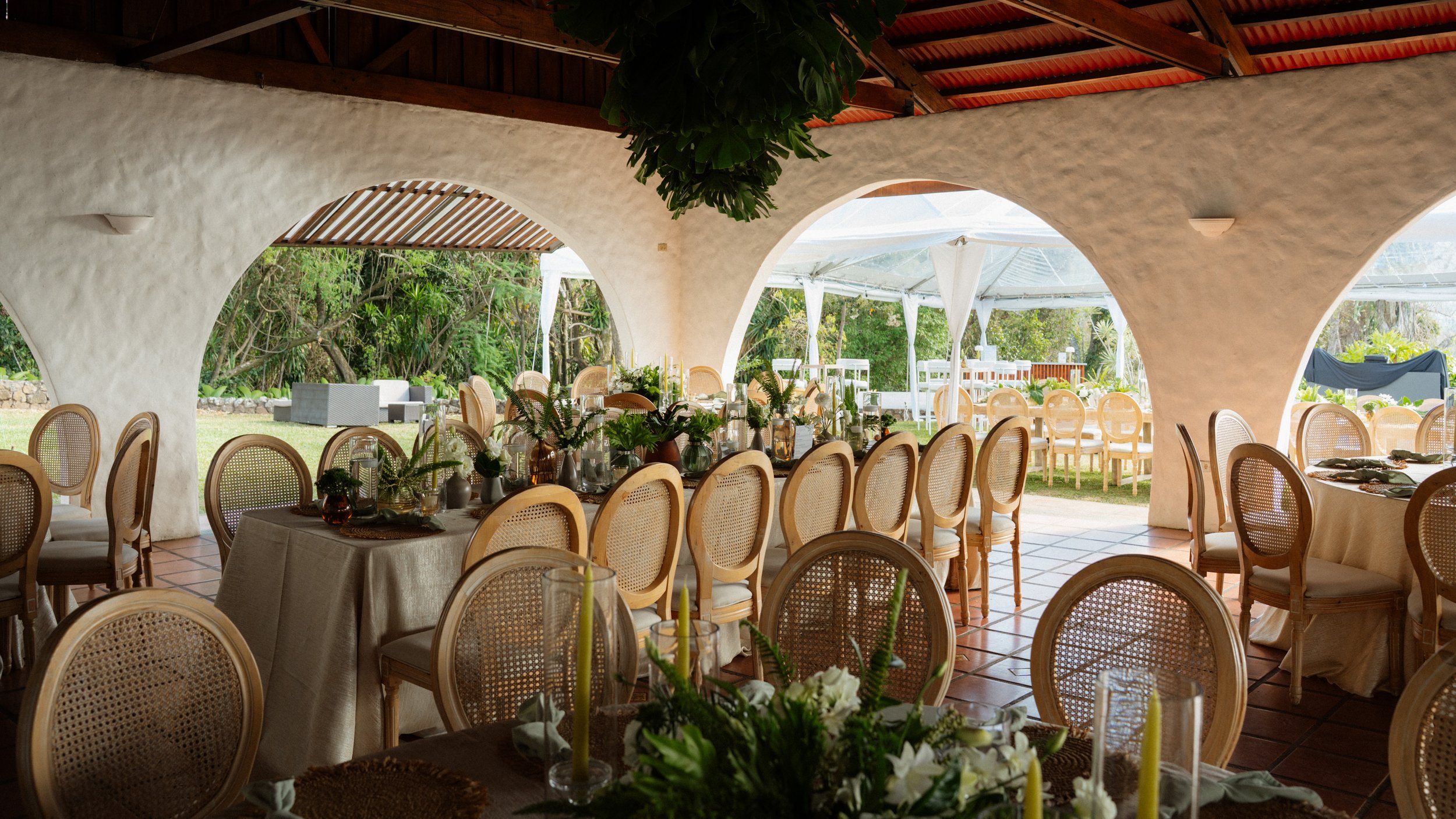 Área de recepción interior con mesas decoradas, sillas de fibras naturales y vista hacia un jardín al aire libre durante una boda en Costa Rica.