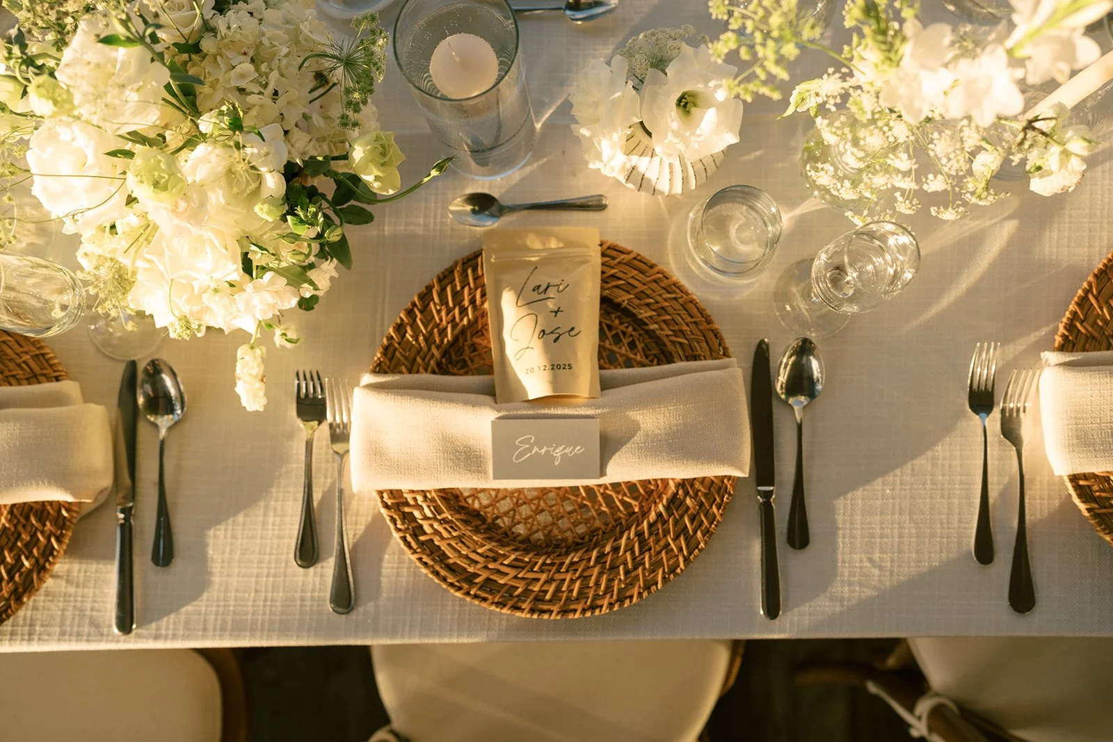 Montaje de mesa para boda con arreglos florales blancos, candelas, texturas naturales y puesto personalizado.