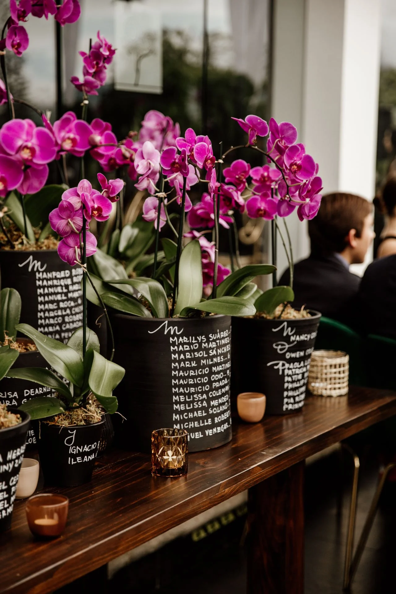 Macetas con orquídeas rosadas y etiquetas escritas a mano sobre una mesa de madera, como detalle decorativo en una boda en Costa Rica.