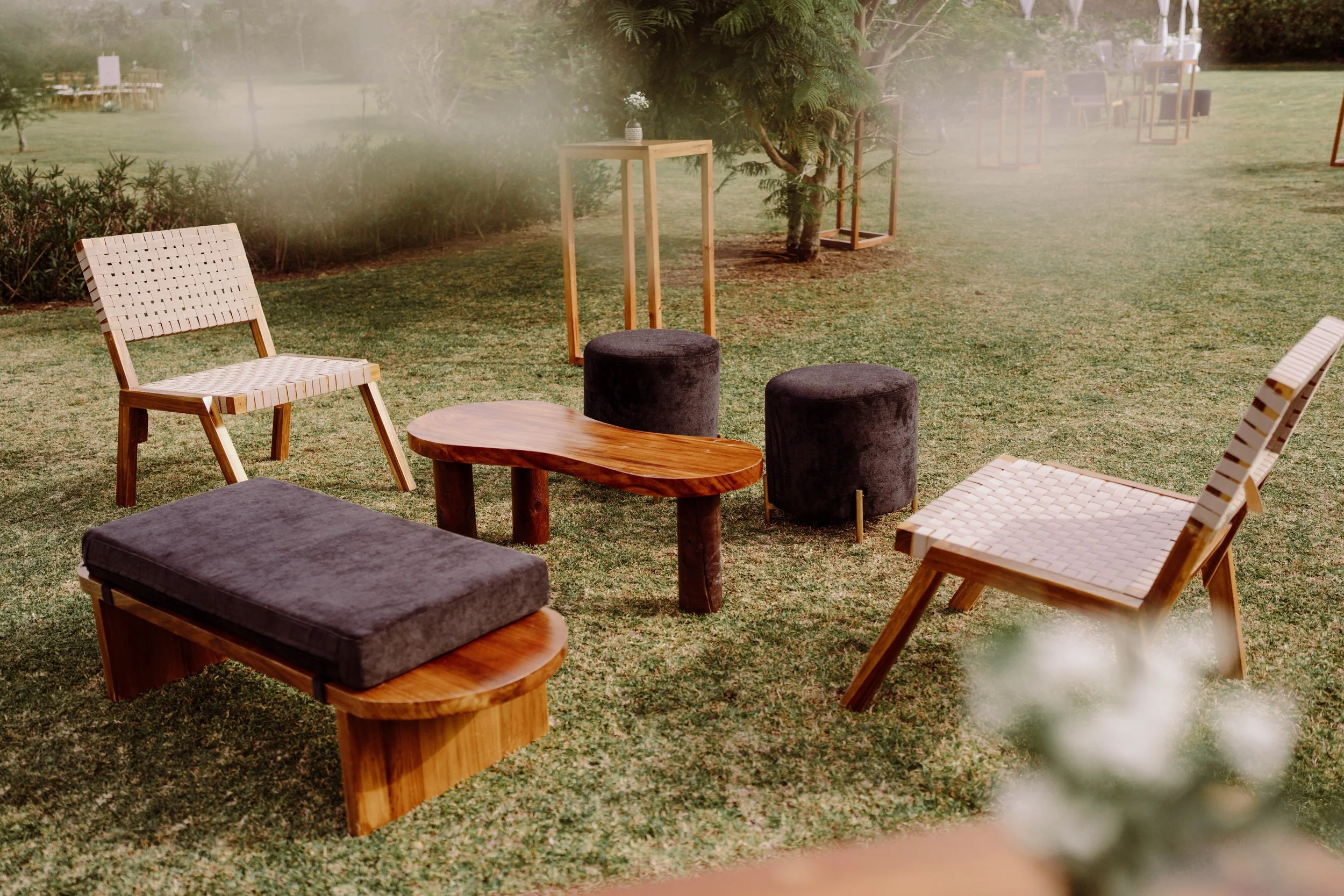 Área lounge al aire libre con sillas de madera, poufs y mesa auxiliar, rodeada de árboles durante una boda en Costa Rica.