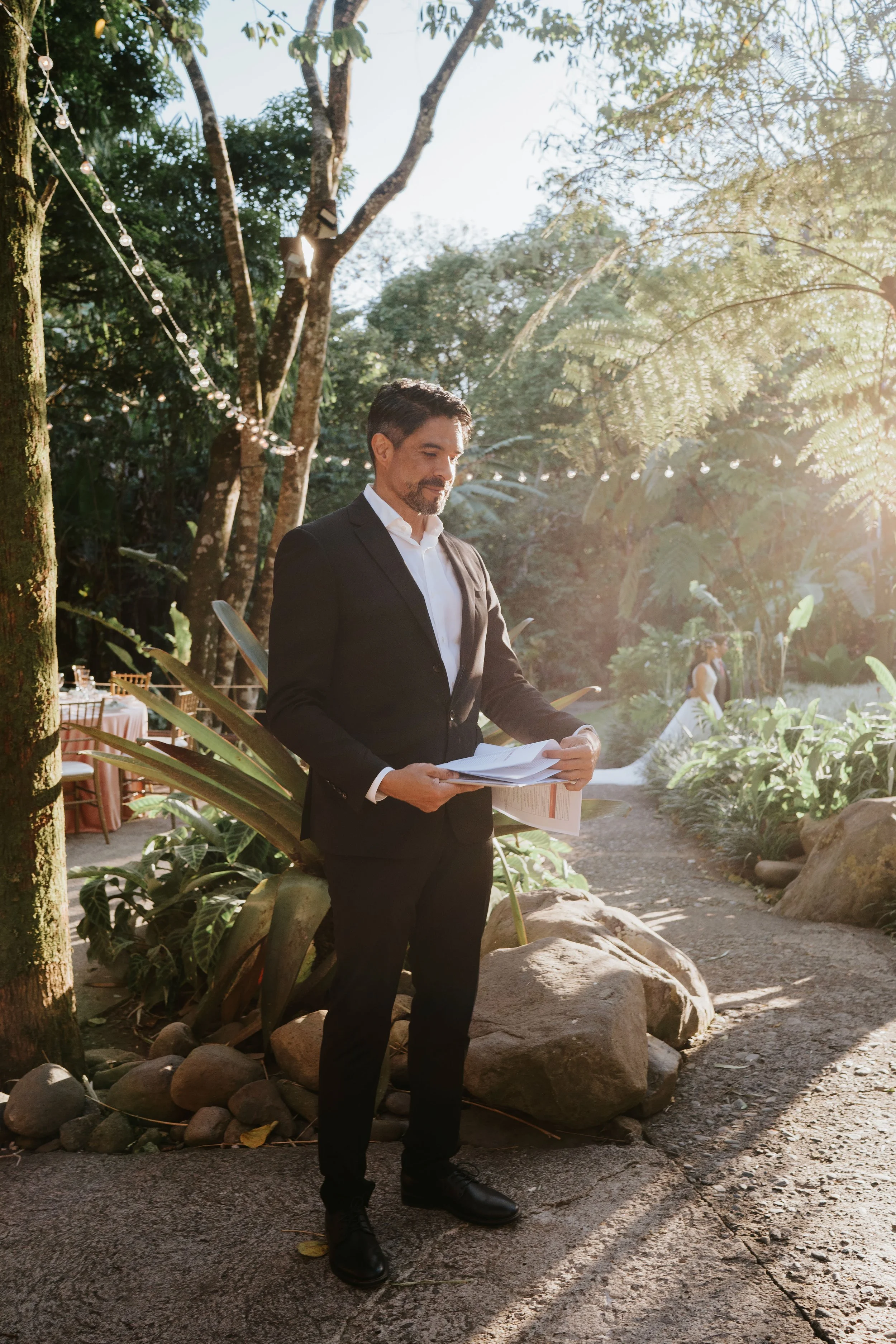 Wedding planner revisando documentos durante una boda al aire libre en Costa Rica, en un espacio rodeado de naturaleza y luces.