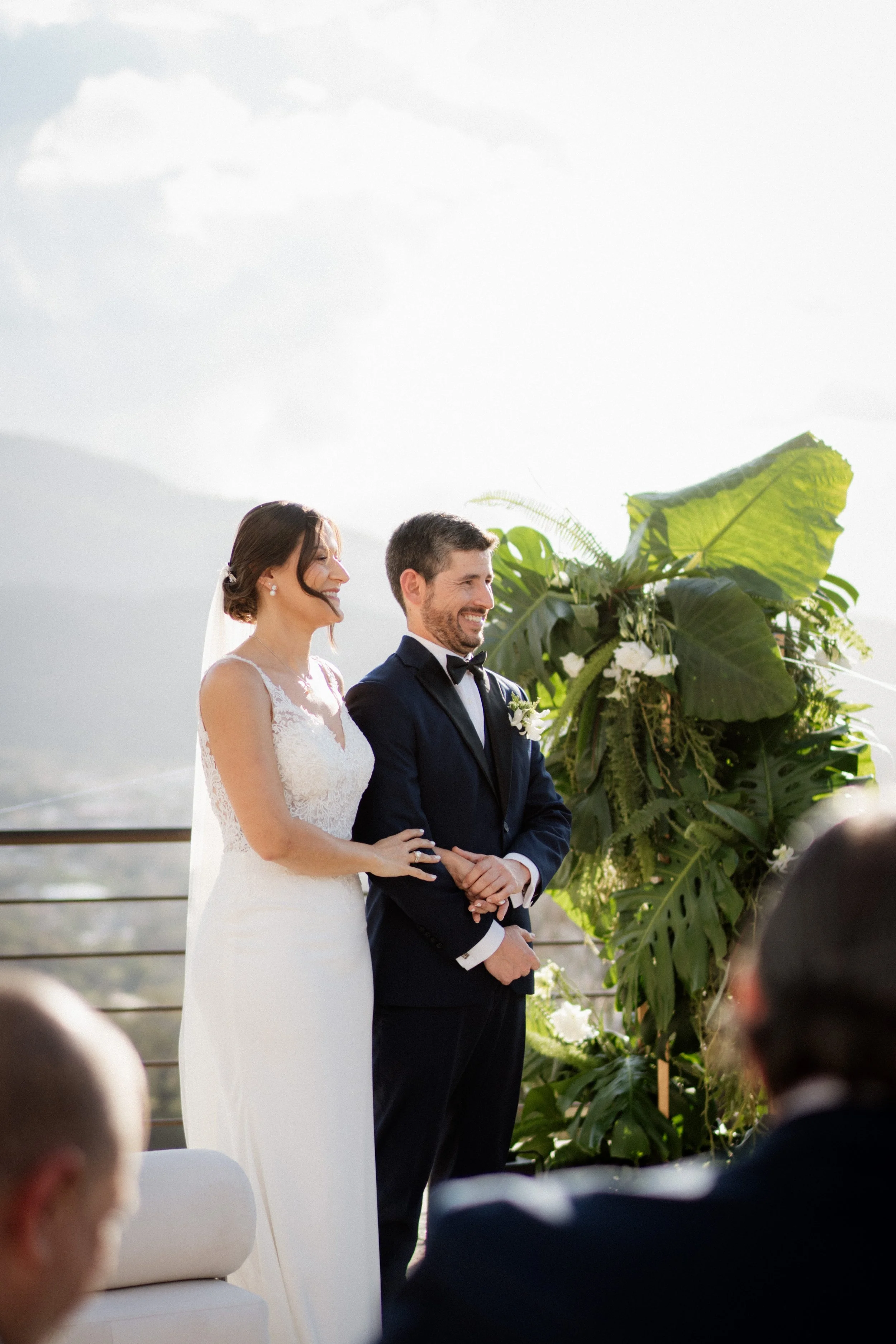 Pareja durante su ceremonia de boda al aire libre, rodeada de hojas grandes, vegetación y luz natural.
