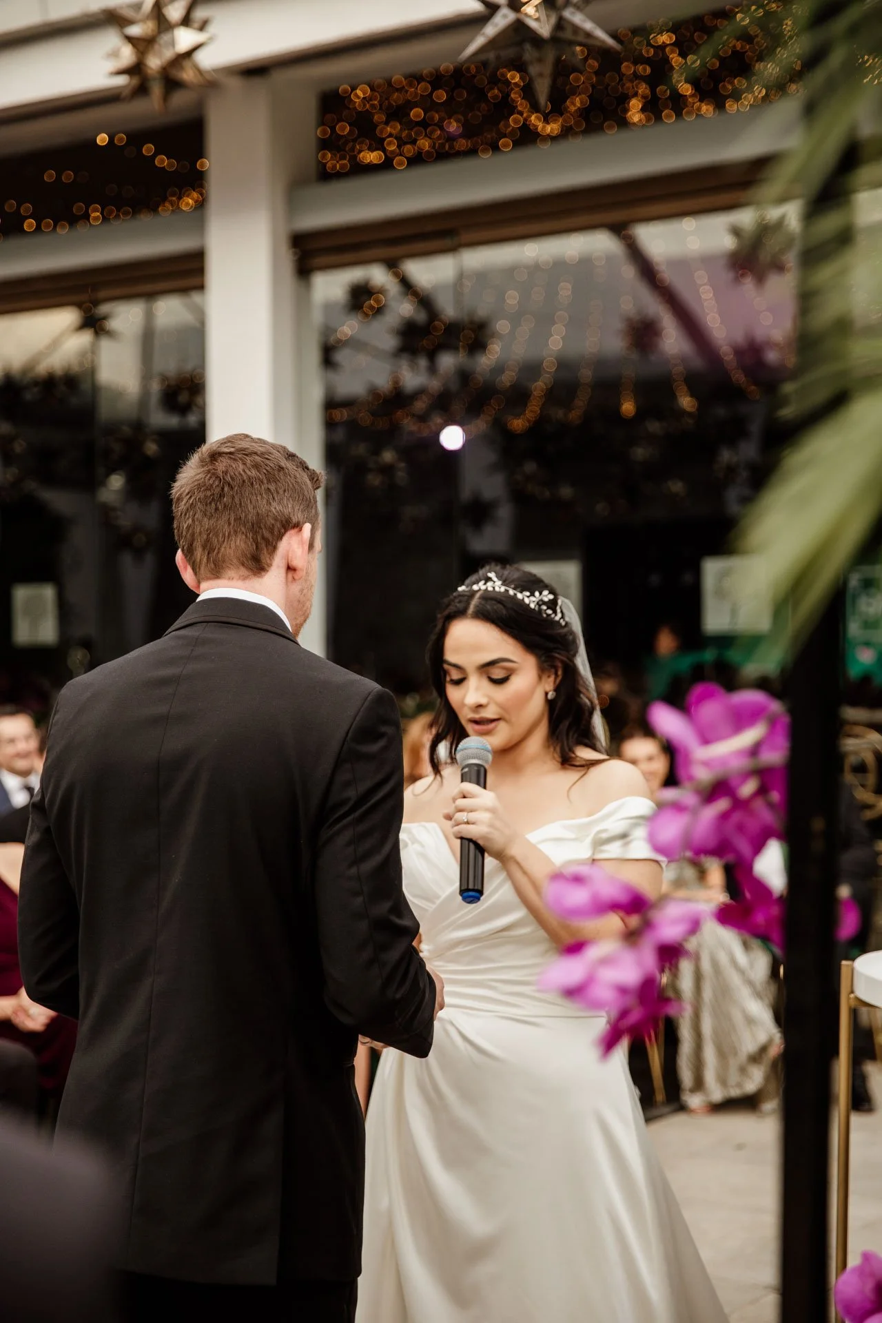 Lectura de votos durante una ceremonia de boda, con los novios frente al altar y una ambientación floral con luces suspendidas.