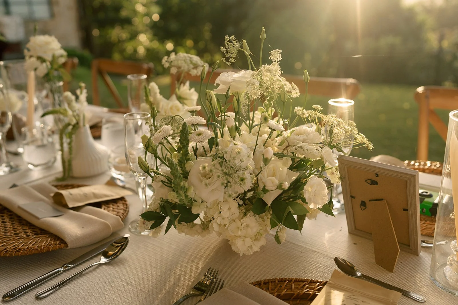 Mesa de recepción al aire libre con centro floral blanco, copas, platos, cubiertos y fotografías decorativas durante una boda en Costa Rica.