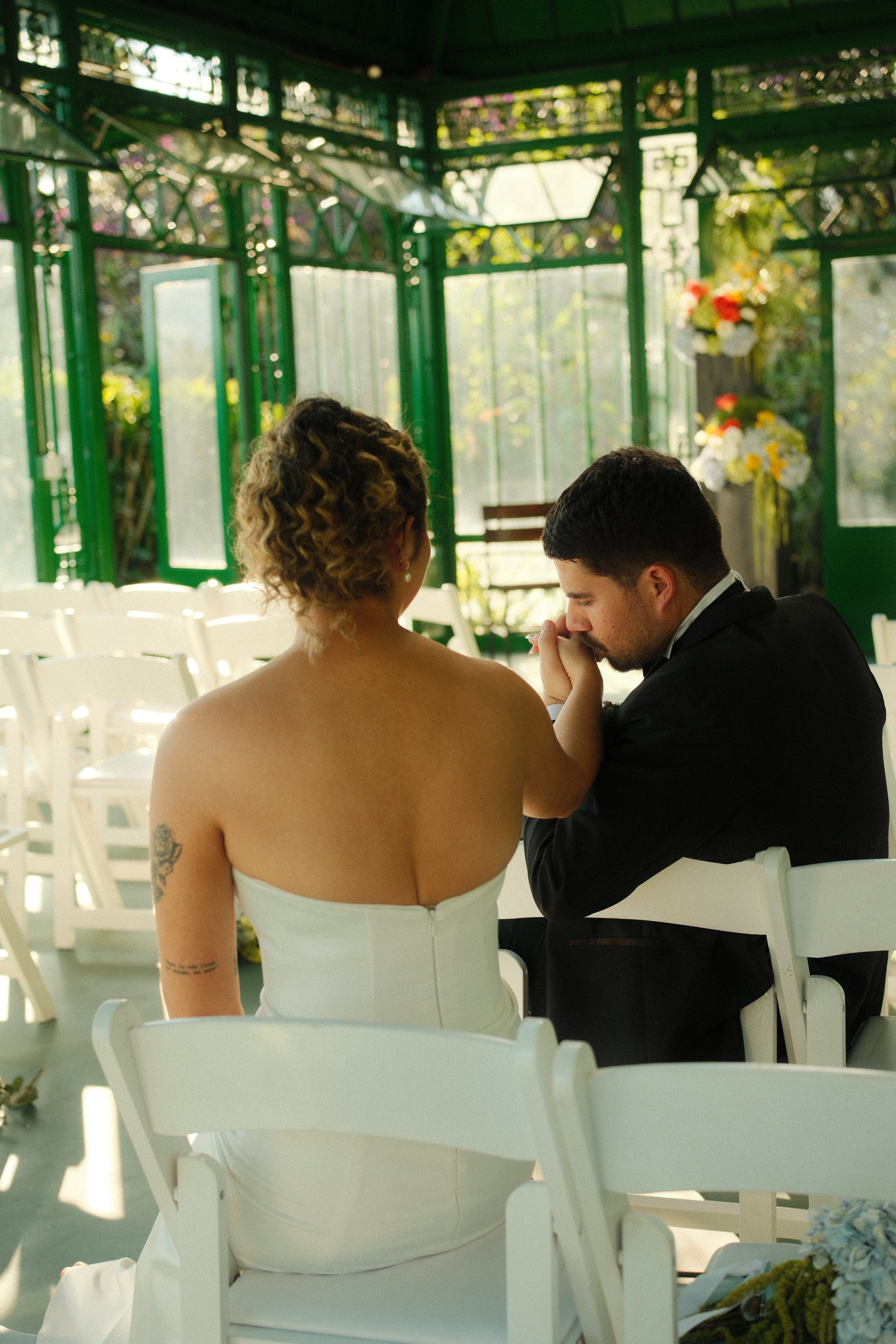 Novios tomados de la mano durante su ceremonia de boda en un pabellón rodeado de flores y vegetación.