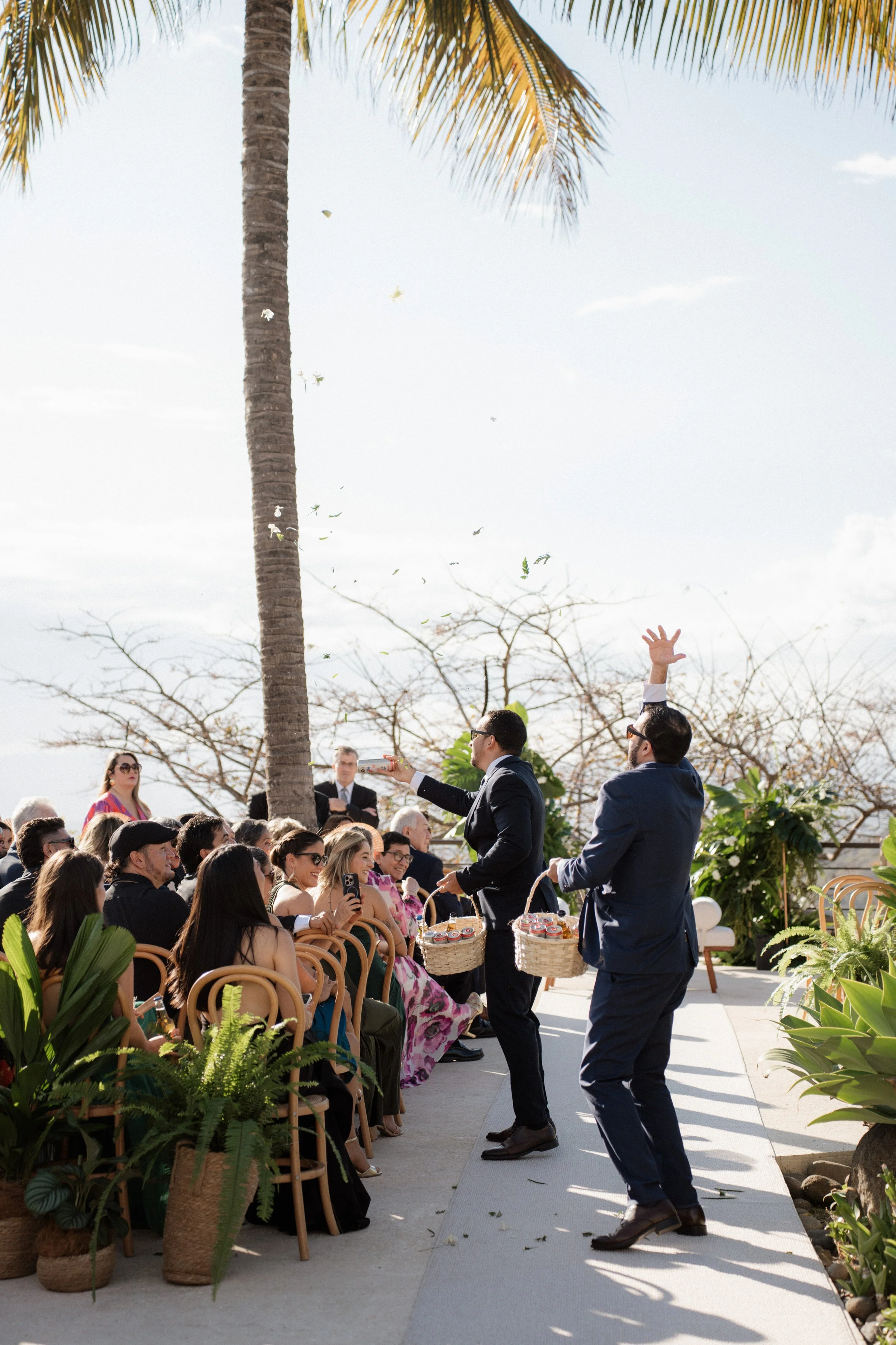 Ceremonia de boda en exterior con invitados, pasillo central y personas caminando hacia el altar bajo un cielo despejado.