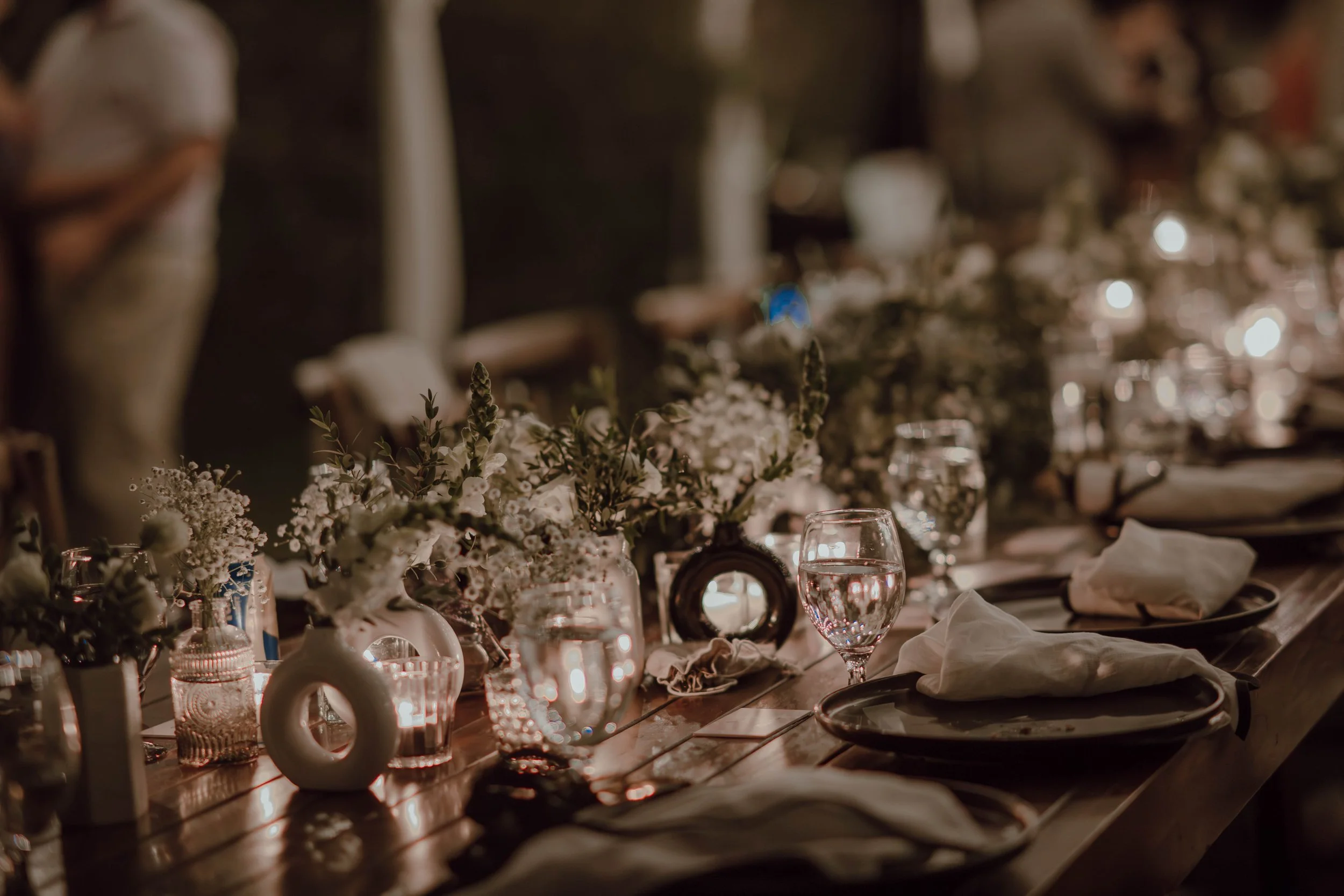 Mesa decorada para una cena de boda, con flores, velas, cristalería y una ambientación cálida de noche.