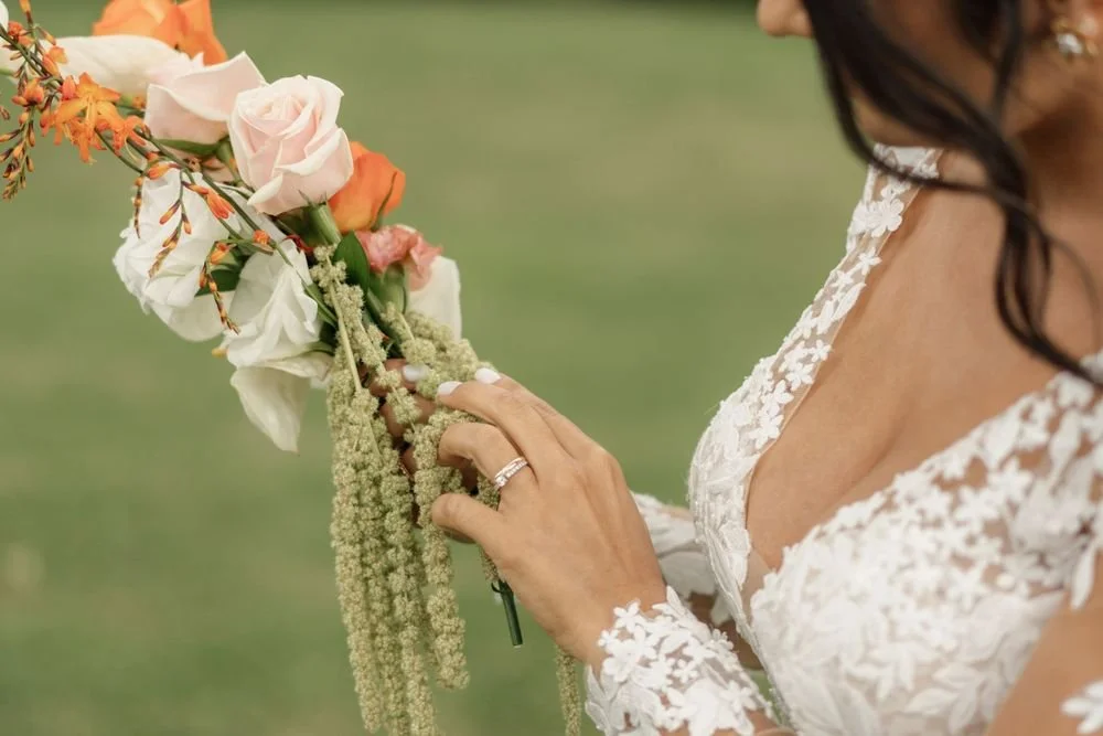 A woman in a wedding dress holding a bouquet of roses, greenery, and flowers outdoors.