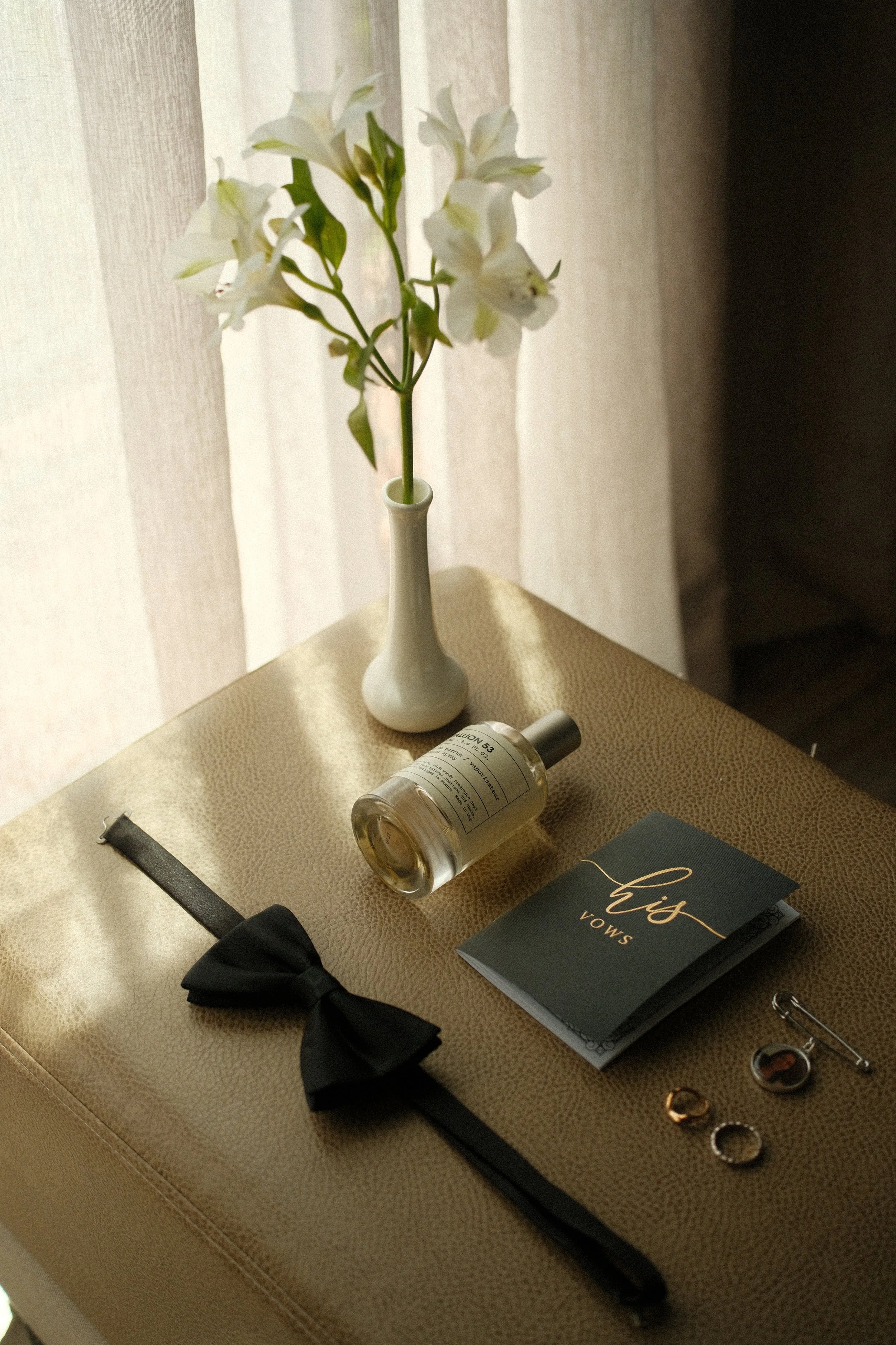 Perfume, corbatín y accesorios personales del novio preparados antes de la boda sobre una superficie texturizada.