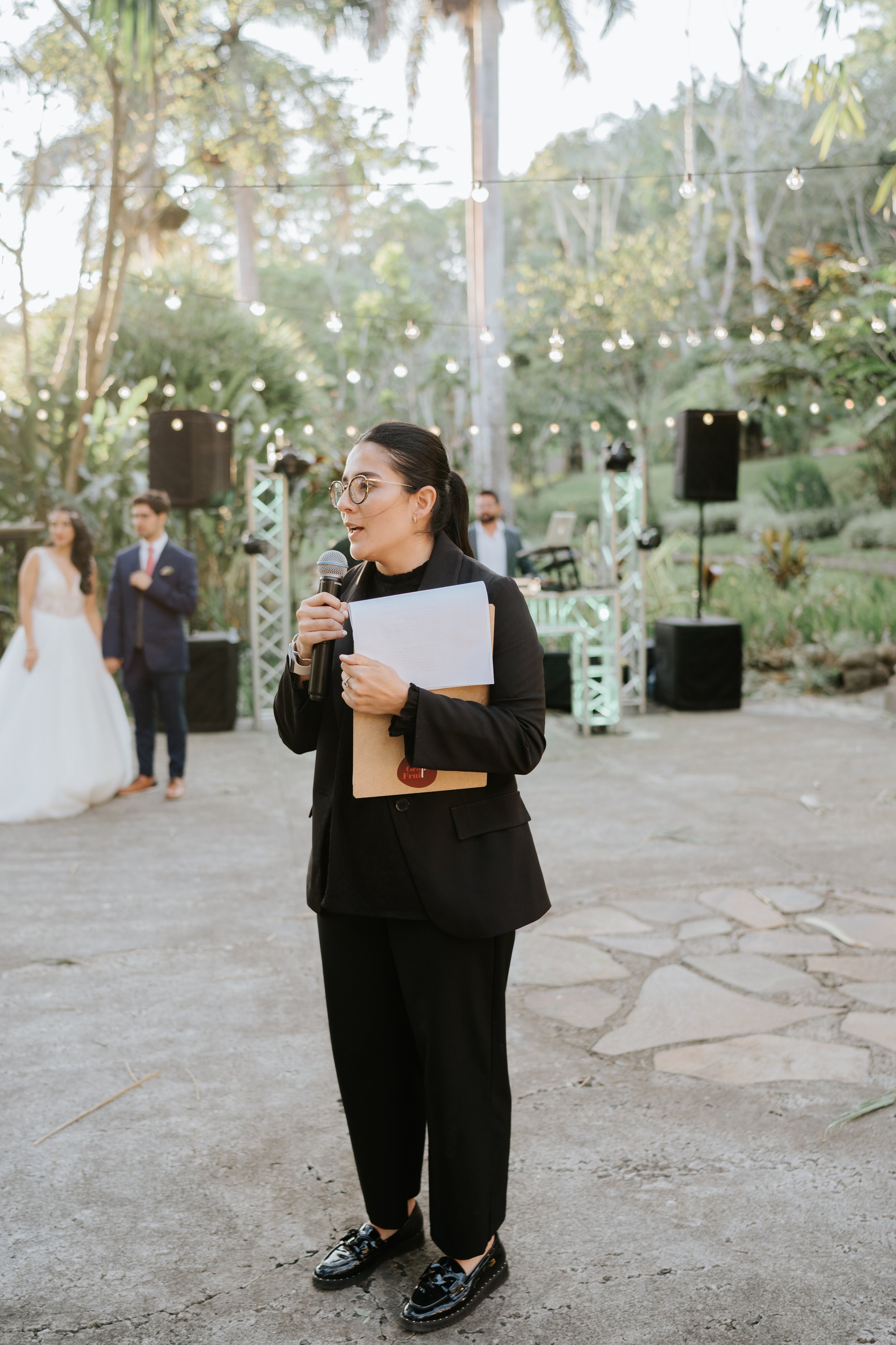 Wedding planner guiando un momento del evento con micrófono y documentos durante una boda al aire libre en Costa Rica.