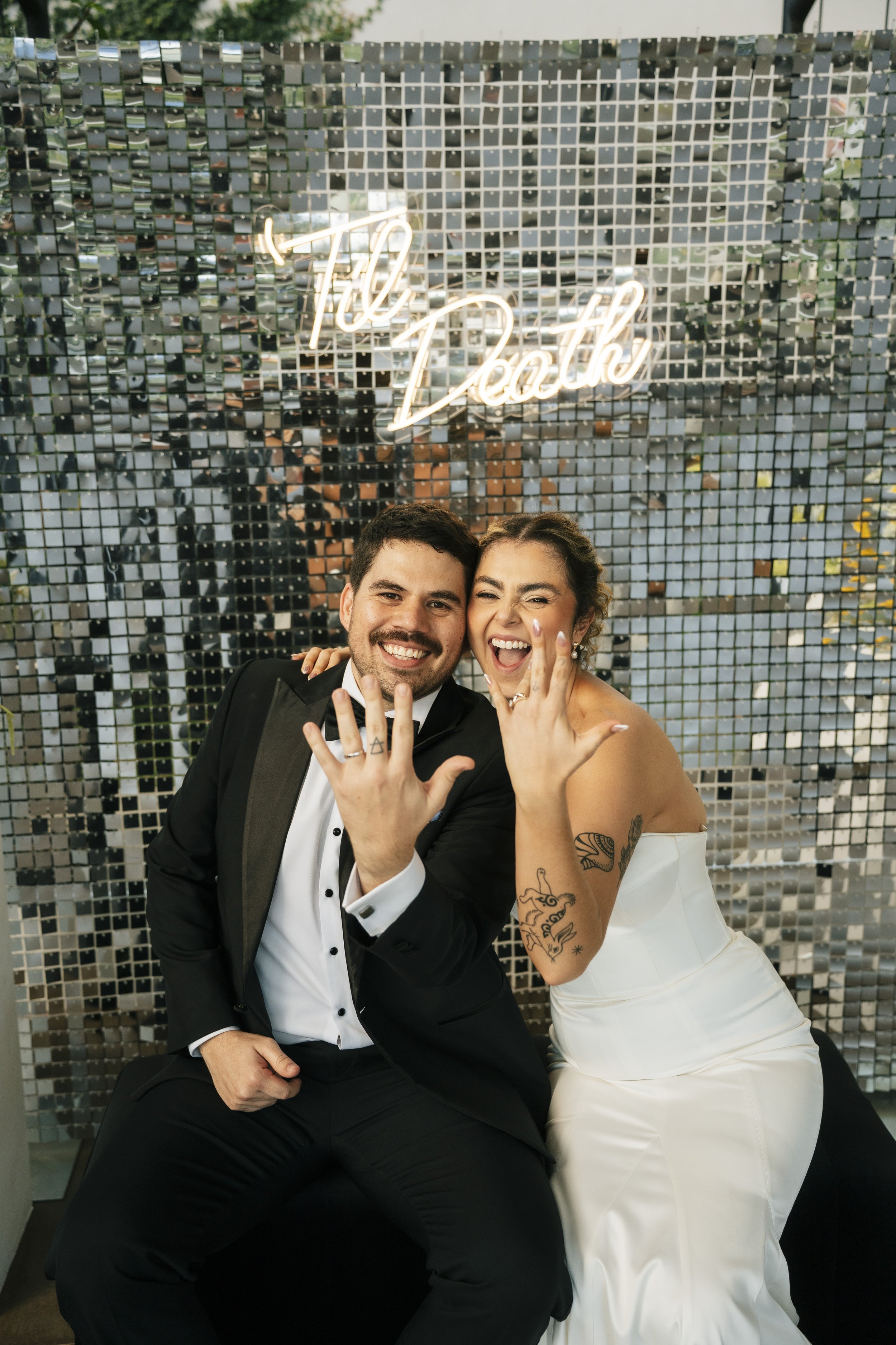 Novios sonriendo frente a un fondo brillante con letrero de neón durante una boda en Costa Rica.