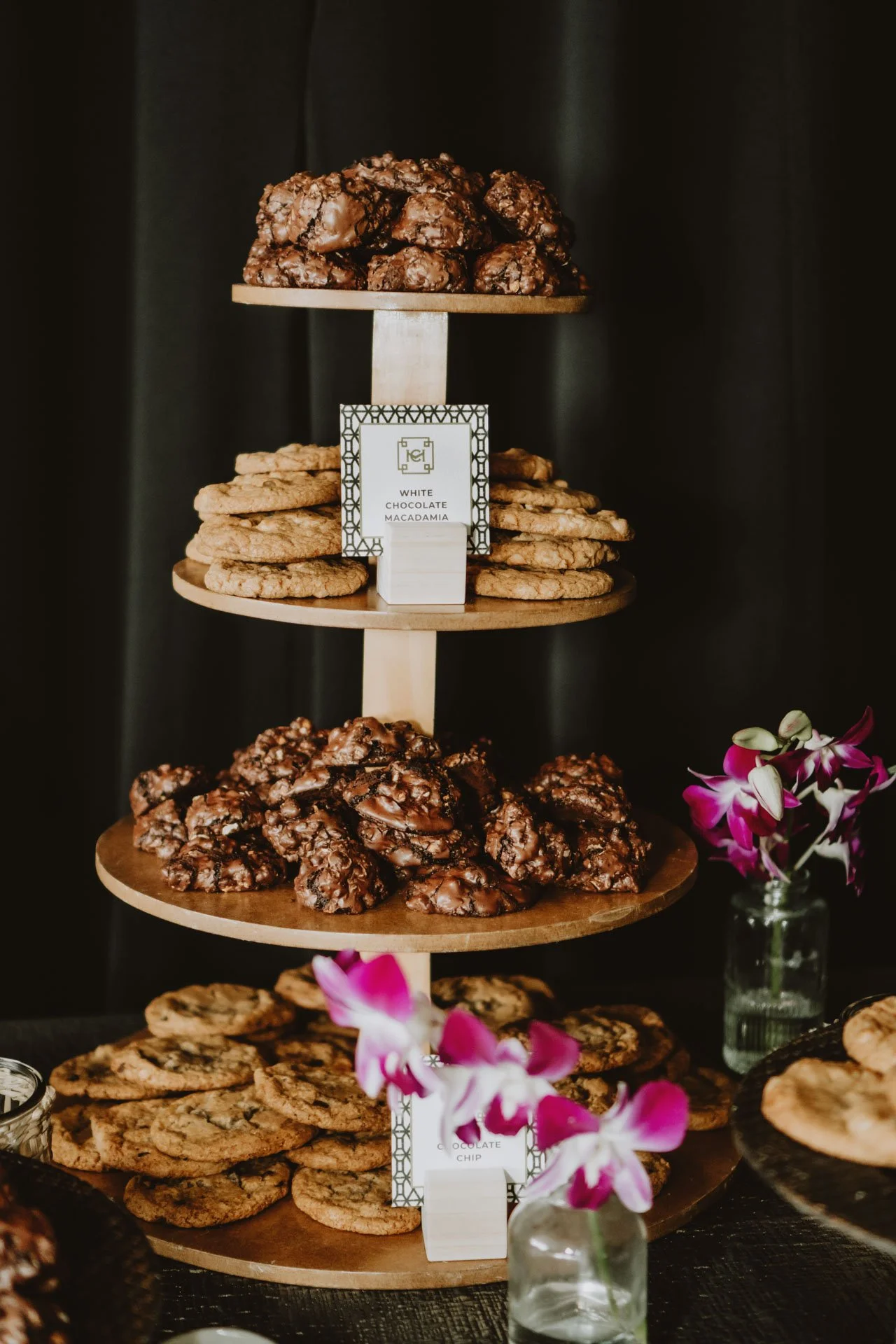 Display de galletas varias en una base de varios niveles, decorado con flores durante una celebración de boda.