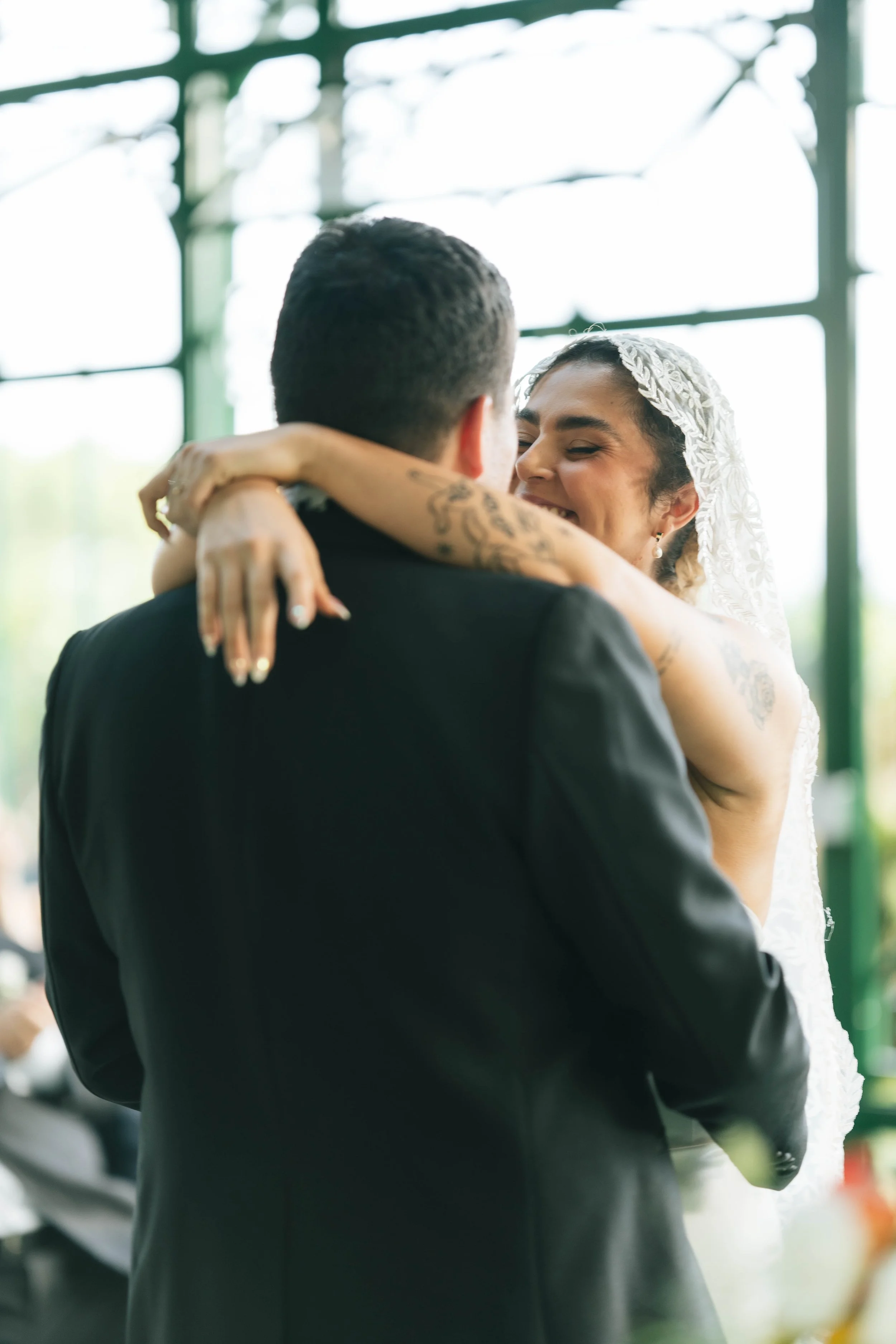 Novia con velo de encaje abrazando al novio durante un momento emotivo de su boda en un espacio interior con luz natural.