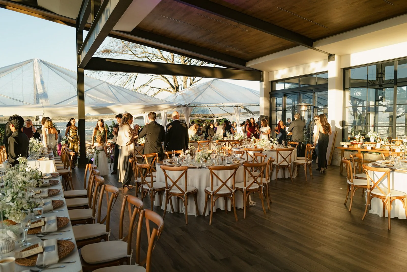 Invitados disfrutando de una celebración en un espacio interior-exterior, con mesas decoradas, vista a la ciudad y ambientación cuidada.