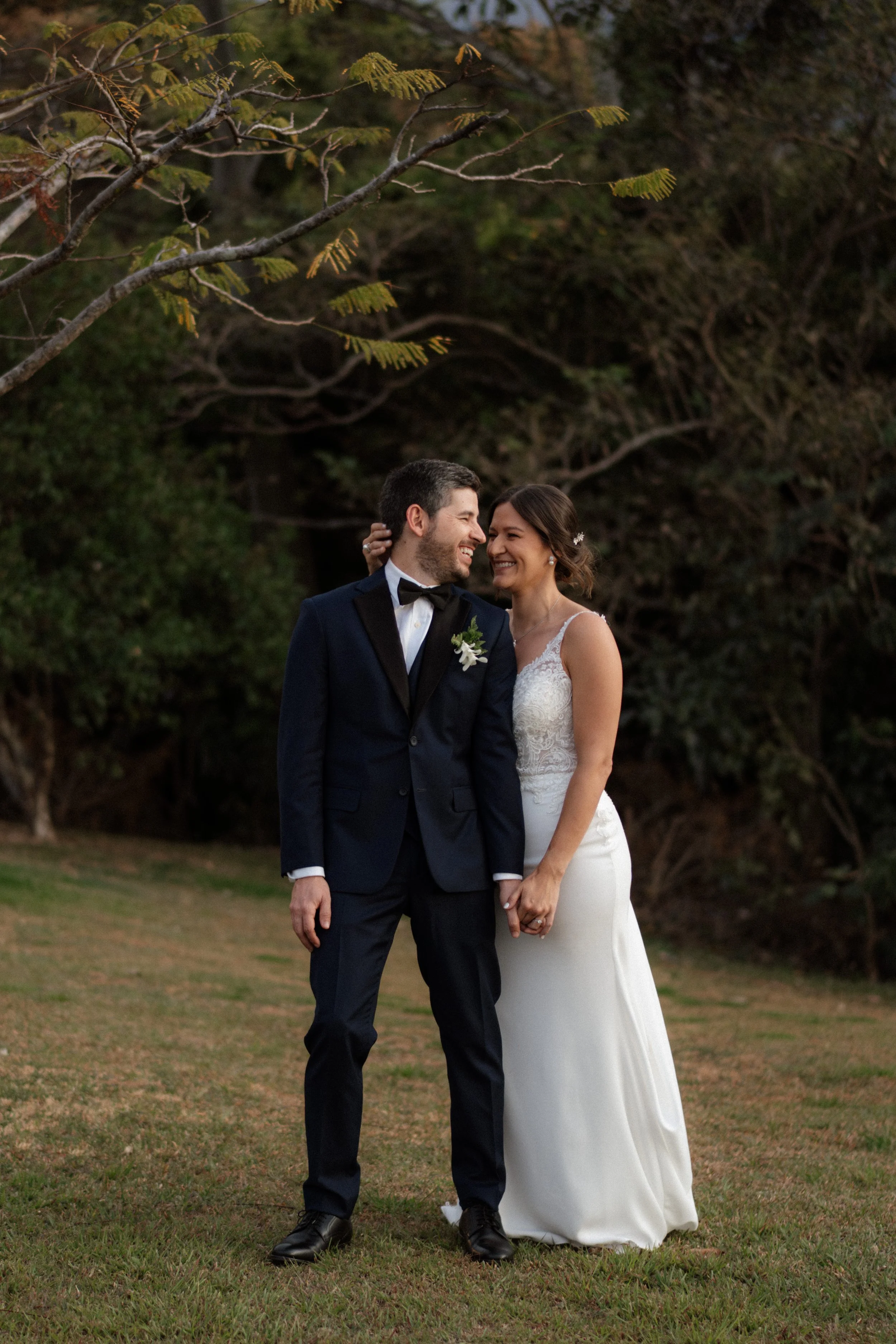 Novios sonriendo y tomados de la mano al aire libre, rodeados de naturaleza durante su boda en Costa Rica.
