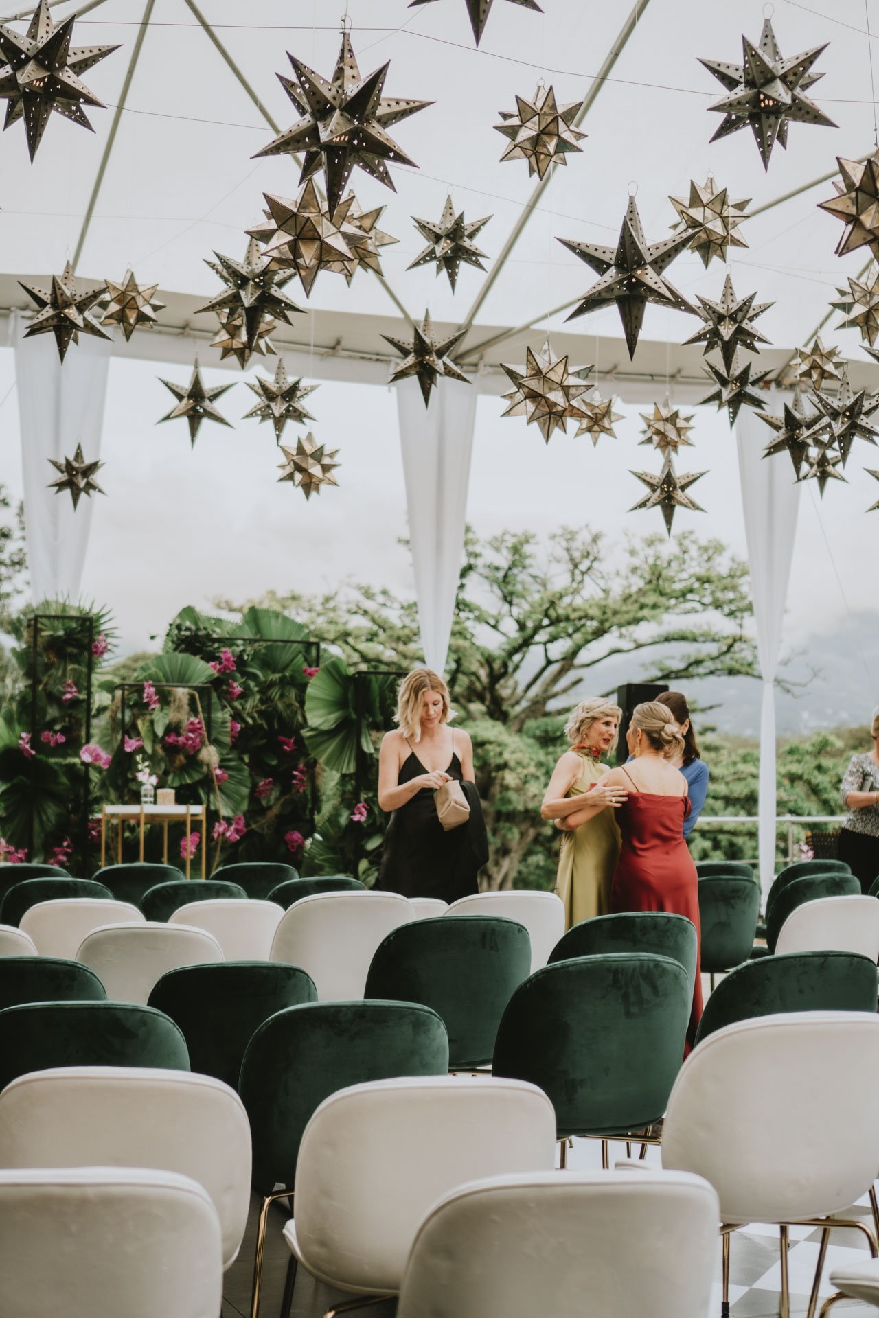 Invitados reunidos en un montaje de ceremonia al aire libre, con sillas en tonos claros y verdes, carpa decorada y naturaleza alrededor.
