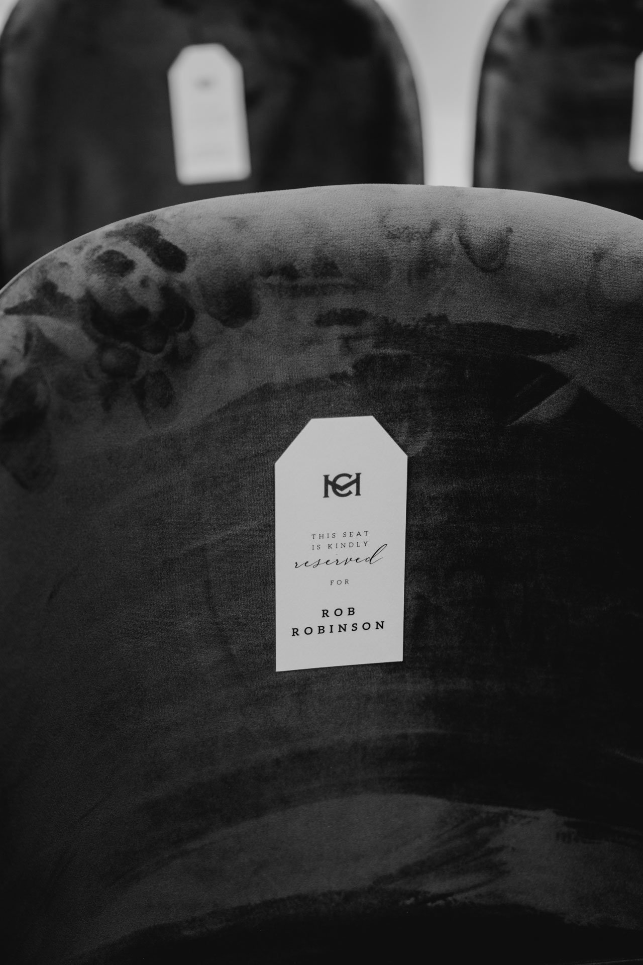 Detalle en blanco y negro de una silla reservada para un invitado especial durante una boda.
