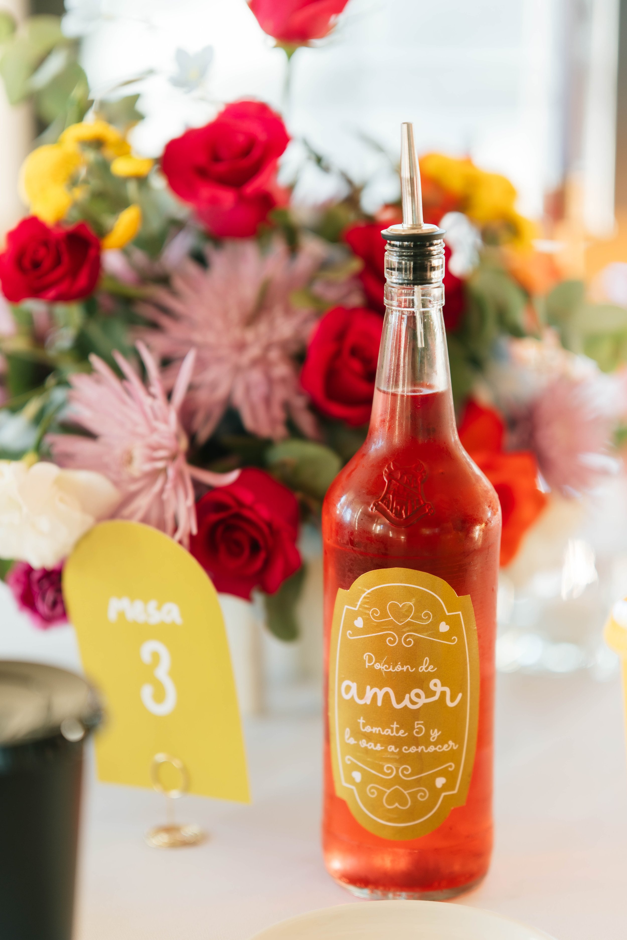 Detalle personalizado de mesa con licor costarricense, flores coloridas y numeración de mesa durante una boda en Costa Rica.