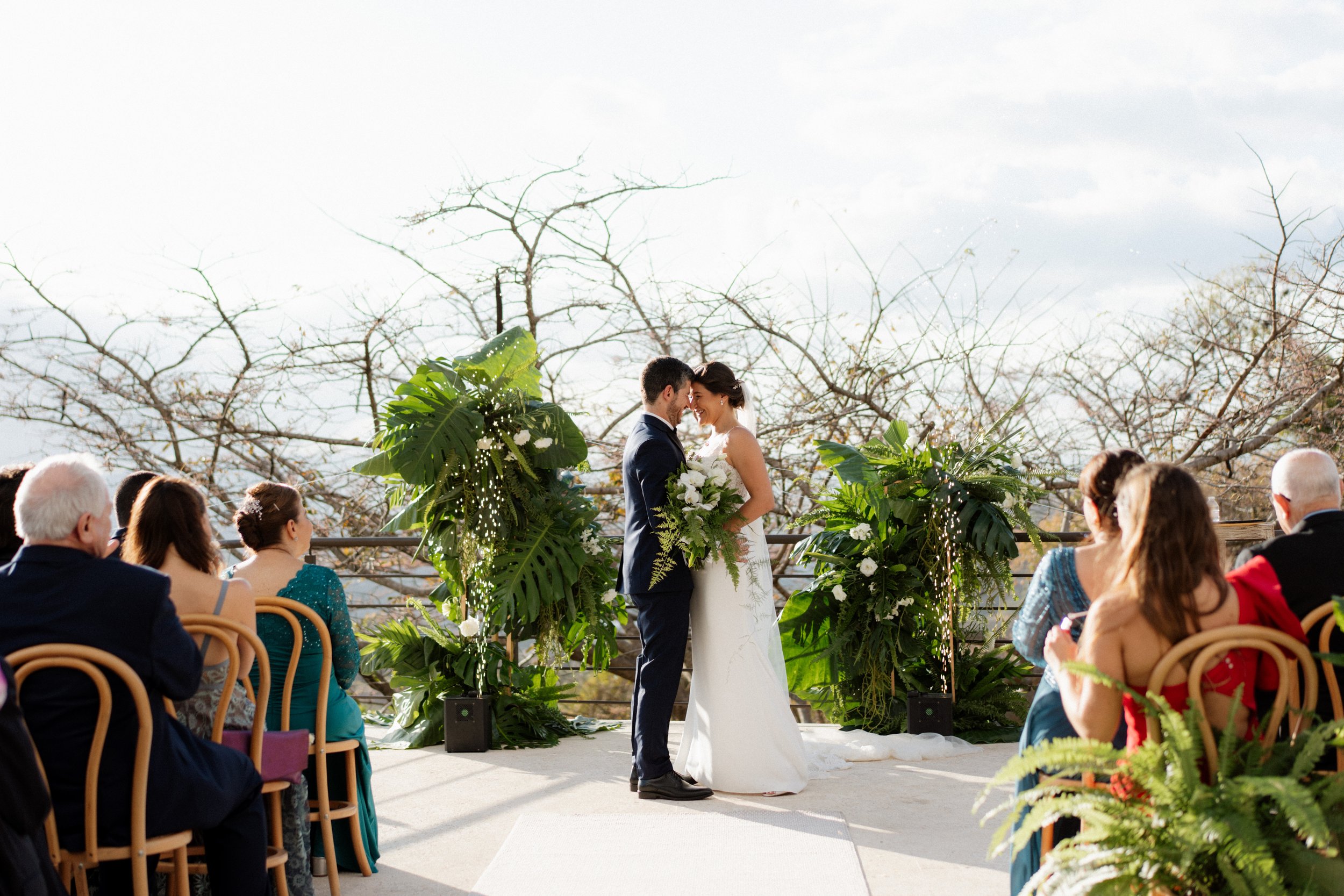 Novios celebrando su ceremonia al aire libre, rodeados de plantas tropicales y de sus invitados en Costa Rica.