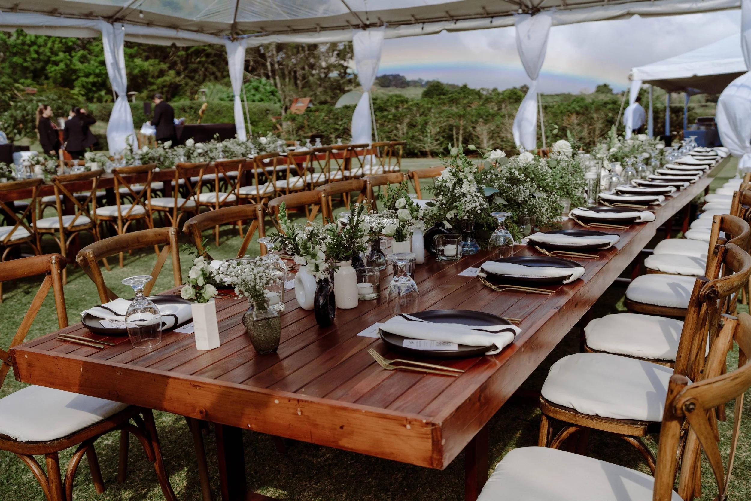 Mesa larga de boda al aire libre bajo carpa, decorada con flores blancas, vajilla y vista al paisaje natural en Costa Rica.