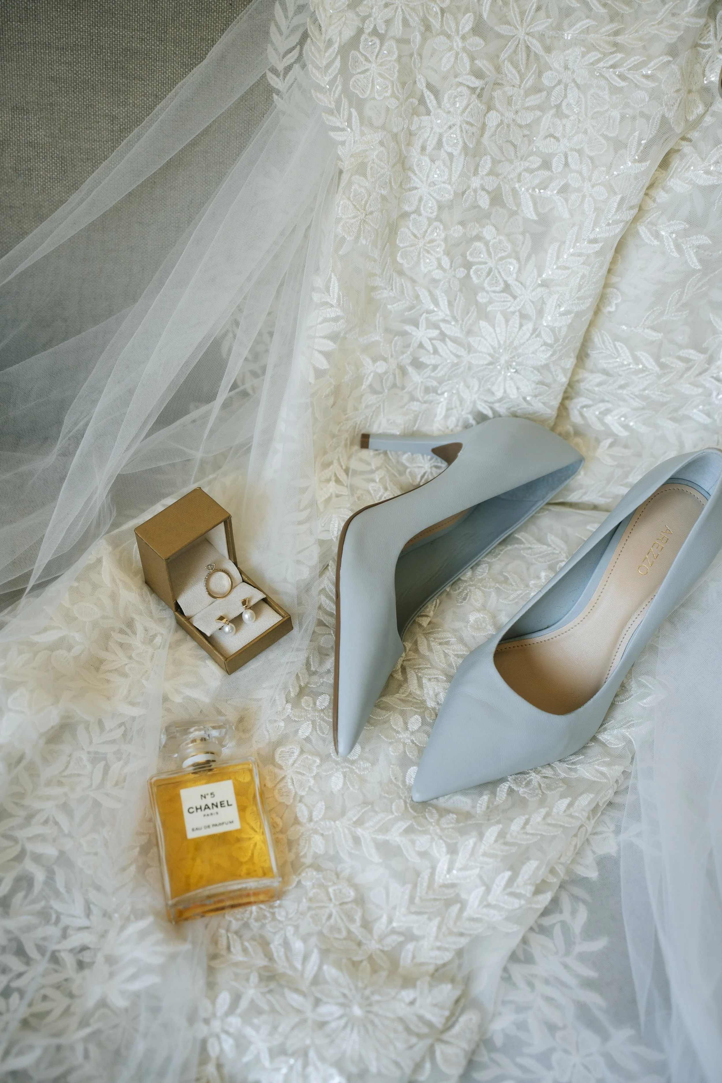 Zapatos de novia, perfume Chanel No. 5 y aretes de perlas preparados durante el getting ready de una boda.