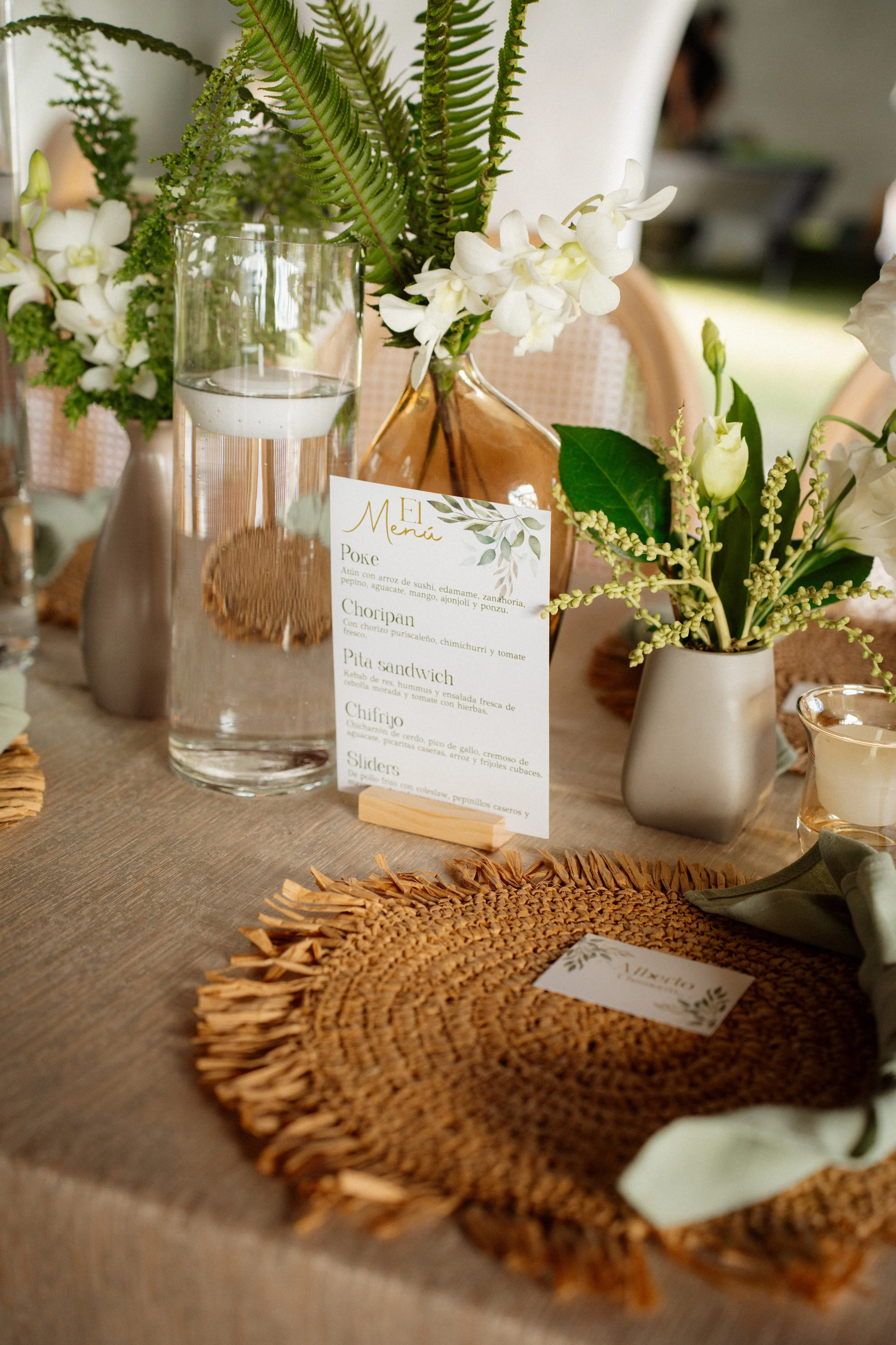 Detalle de mesa decorada con flores blancas y follajes verdes, menú, cristalería y texturas naturales durante una boda en Costa Rica.
