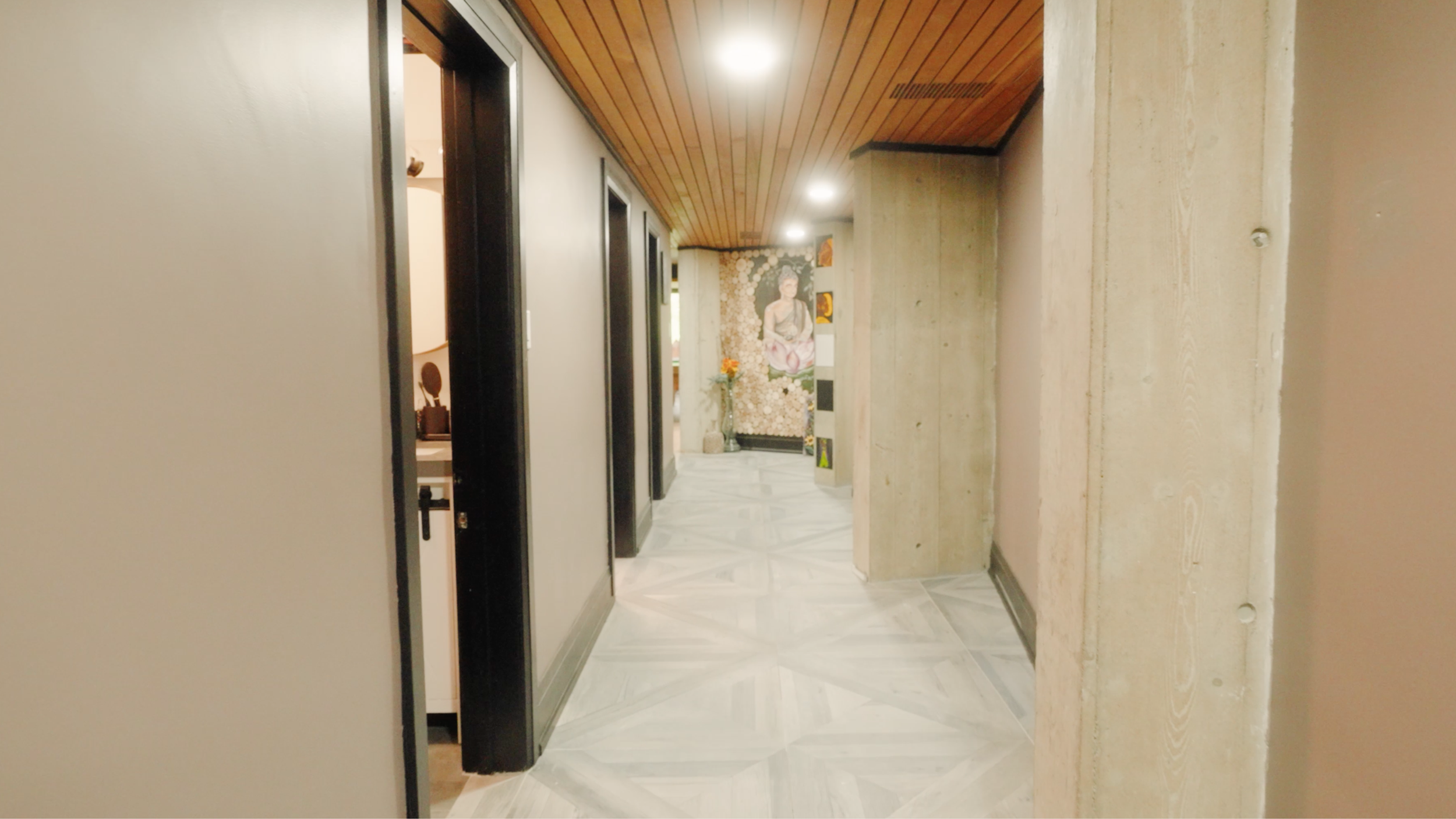 Interior hallway with marble flooring, wooden ceiling, and a Buddha mural at the end, decorated with vases and artwork.