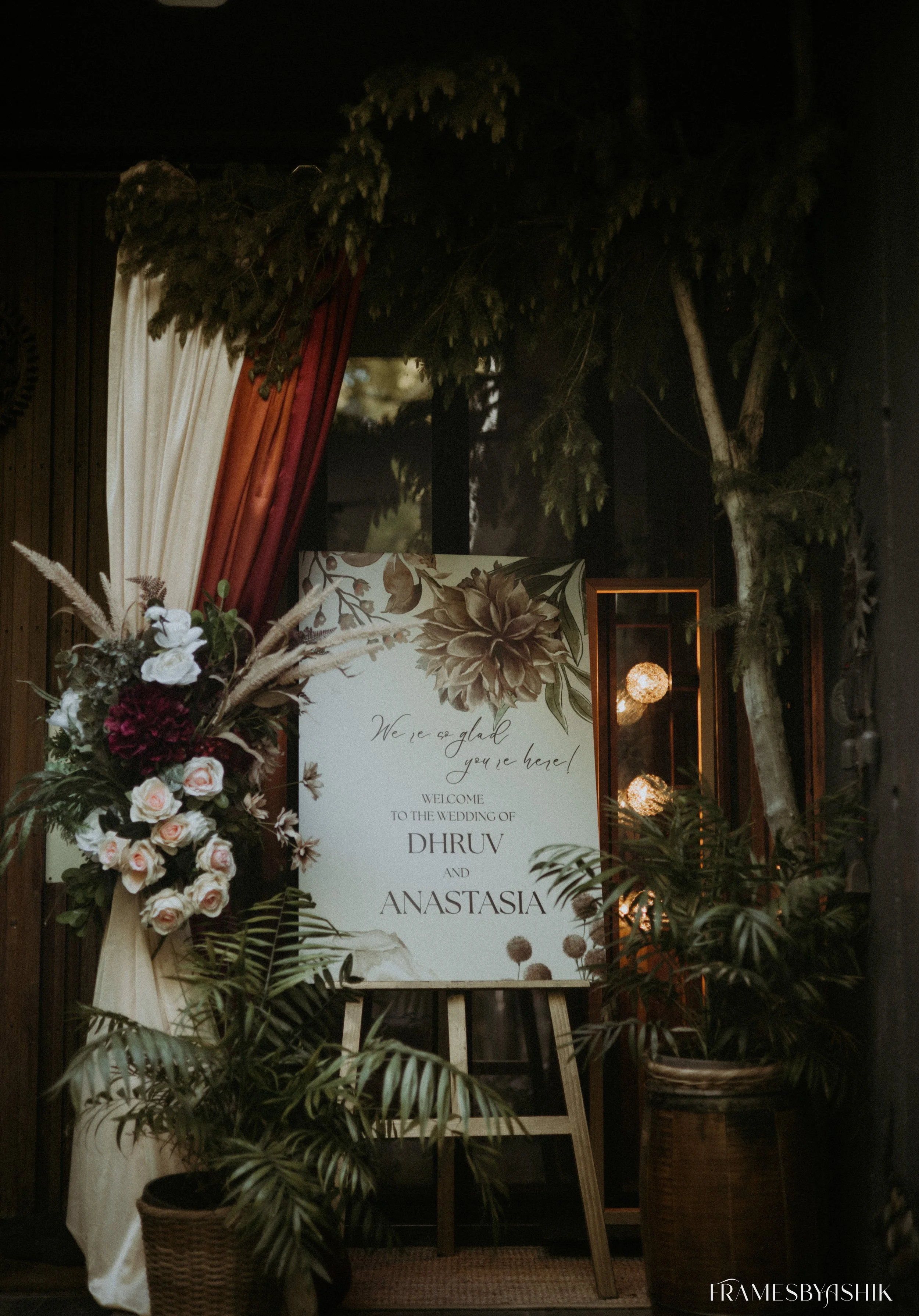 Wedding welcome sign with floral decorations and plants.