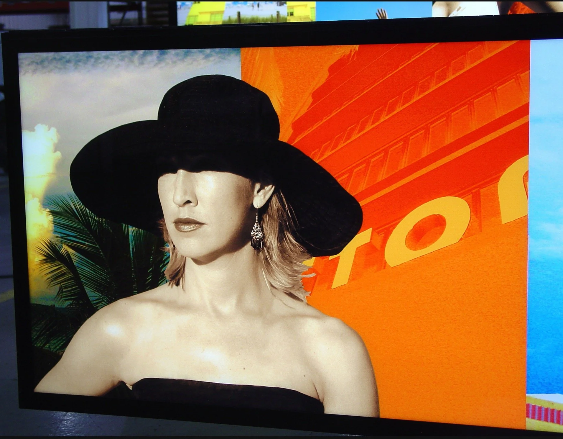 A woman with fair skin and blonde hair wearing a large black hat and earrings, posing with a tropical background including palm leaves and a sunset, and an orange and yellow backdrop with text.