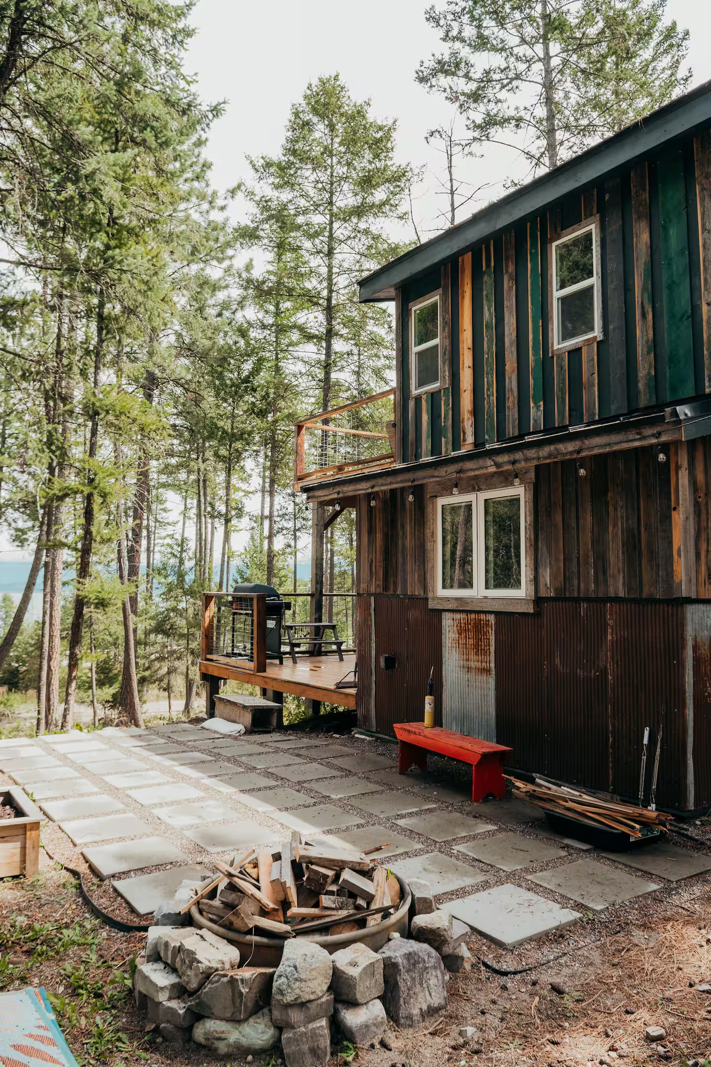 Backyard area undergoing construction with a stone fire ring, concrete pavers, and a rustic wooden house surrounded by trees.