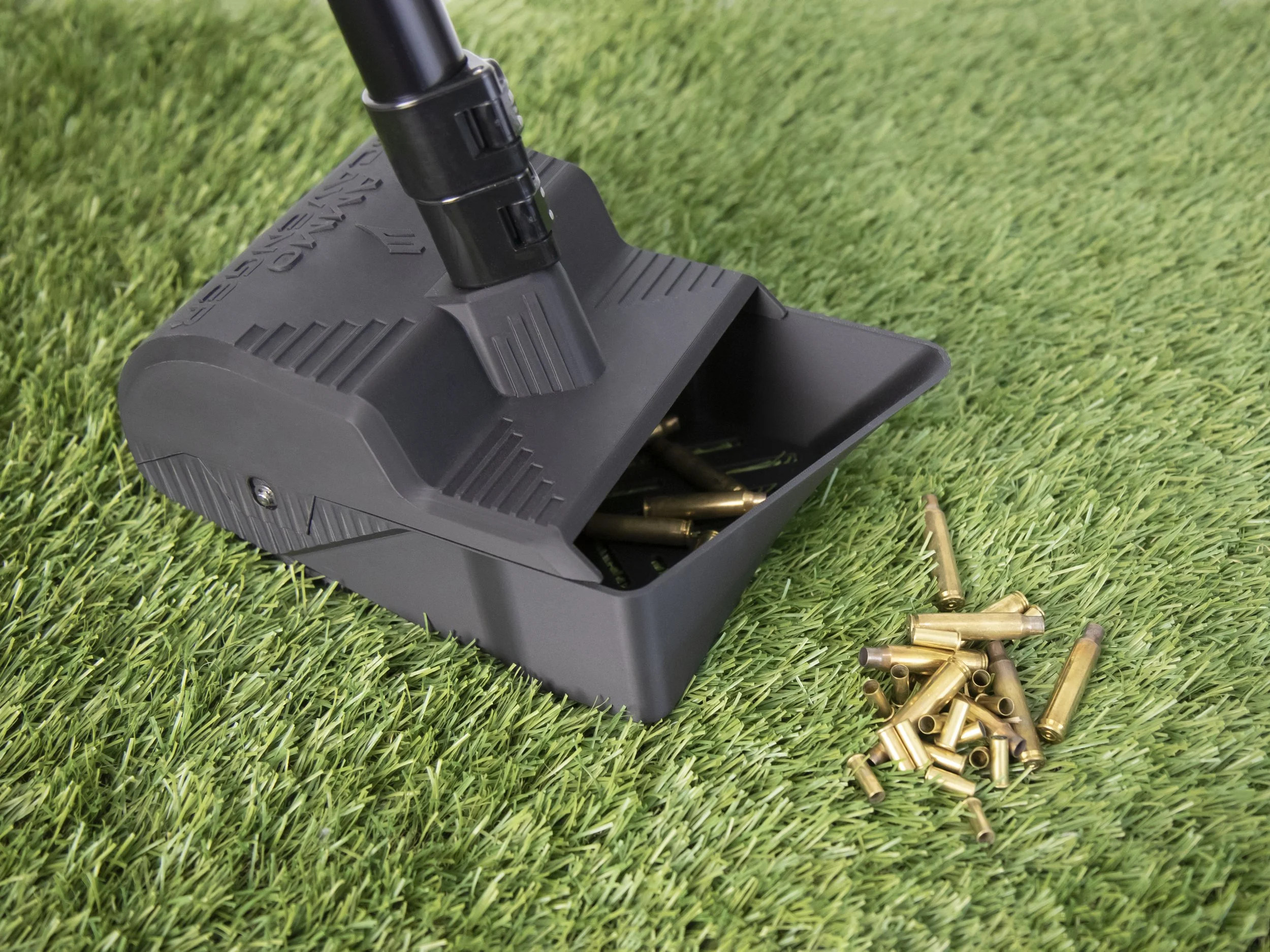 The grass scavenger, a tool used to pick up spent brass cases off grass, sitting on grass with a pile of cases next to it.