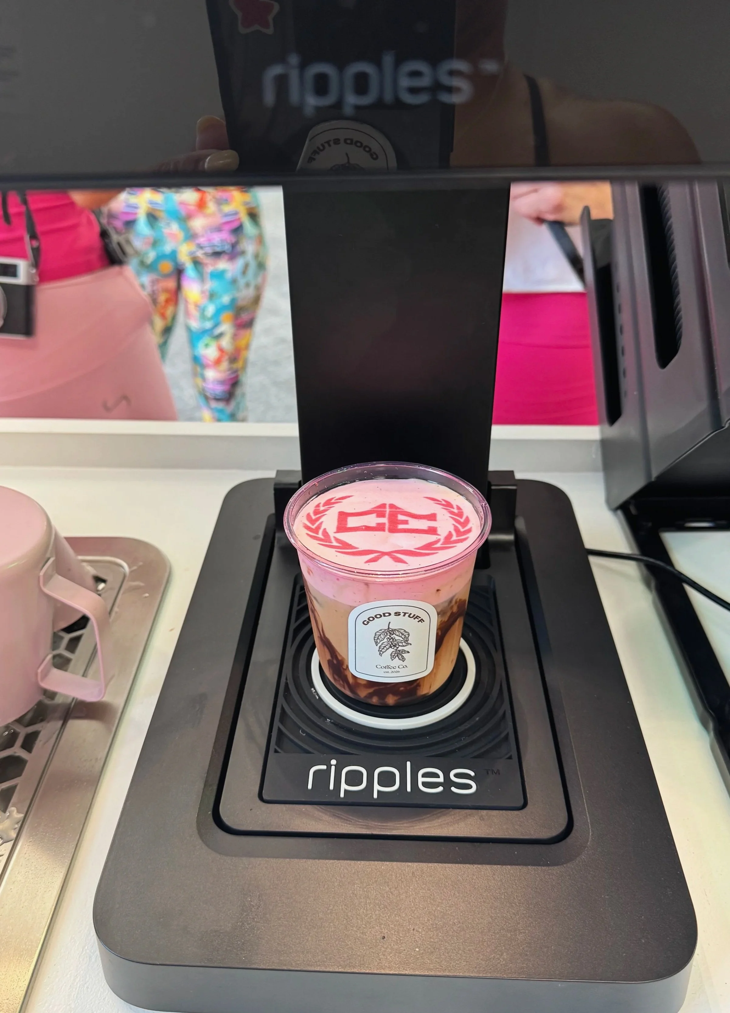 Pink bubble tea with a lid that has a red logo and a black straw on a Black and gray Ripple's branded coffee warmer.