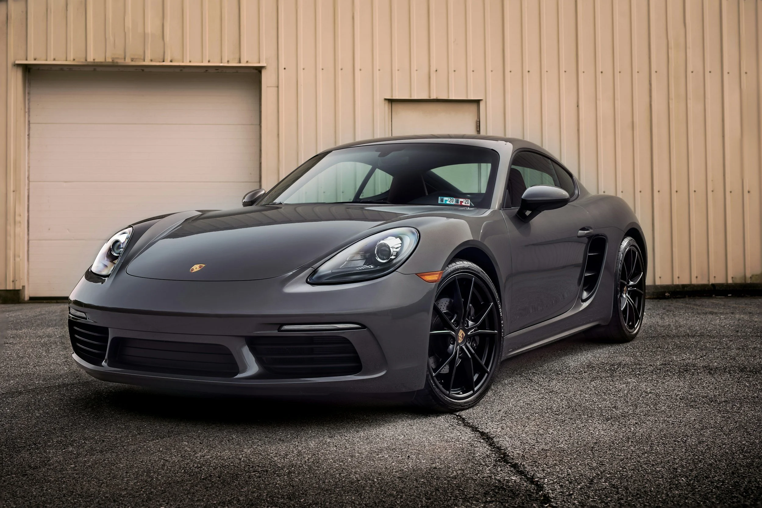 A gray Porsche sports car parked in front of a beige industrial building with a garage door.