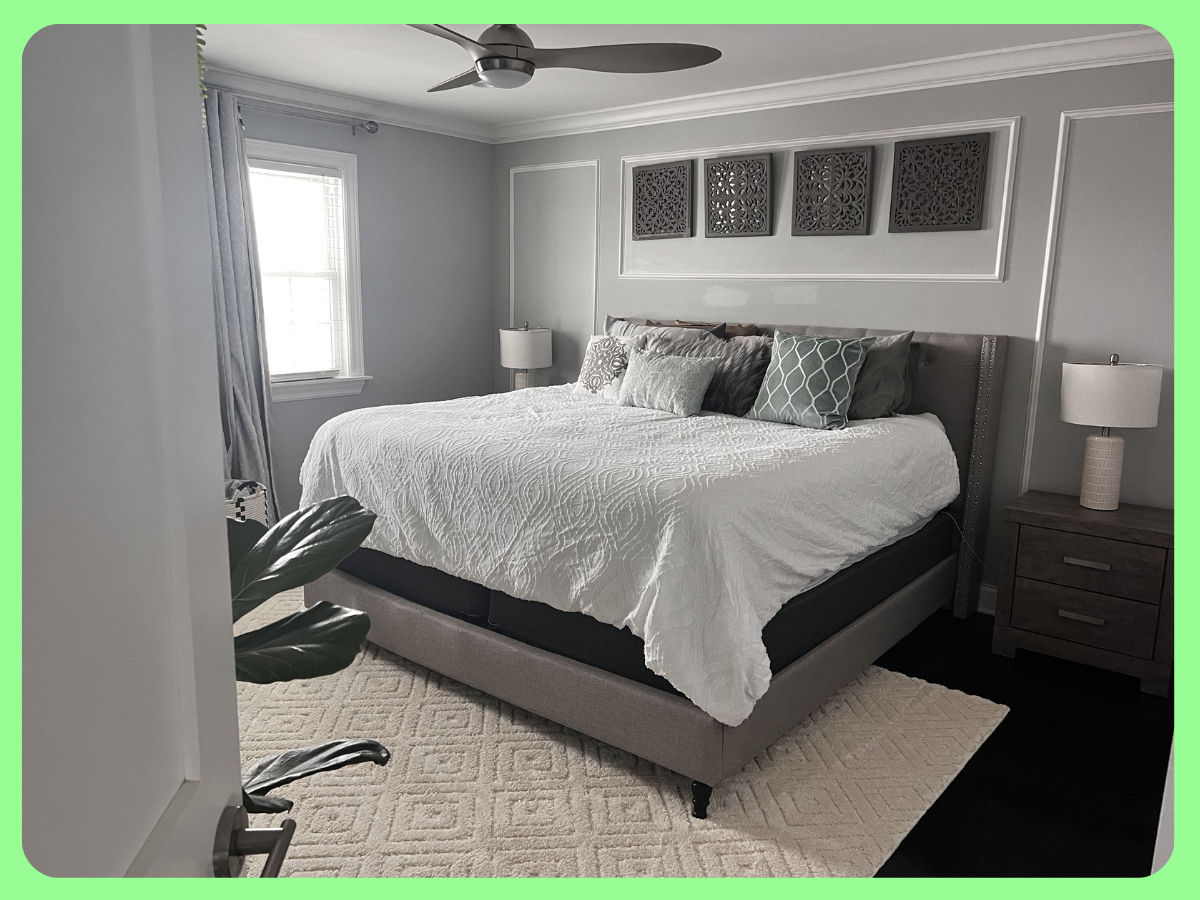 A modern bedroom with a large bed, white bedding, decorative pillows, nightstands with lamps, a window with curtains, and wall art above the bed.