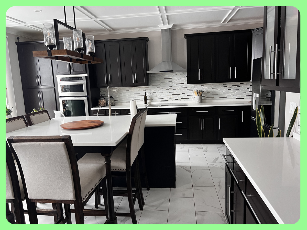 Modern kitchen with black cabinets, white countertops, and a tiled backsplash, featuring a kitchen island with a wooden tray, dining chairs, and a pendant light fixture.
