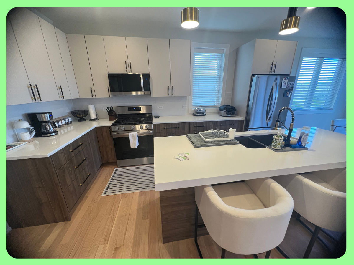 Modern kitchen with white upper cabinets, dark wood lower cabinets, stainless steel appliances, a white island with bar chairs, and hardwood flooring.