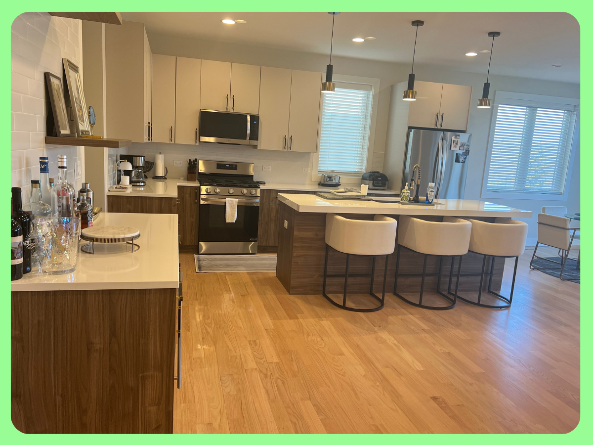 Modern kitchen with hardwood floors, white cabinetry, stainless steel appliances, and an island with four beige barstools.