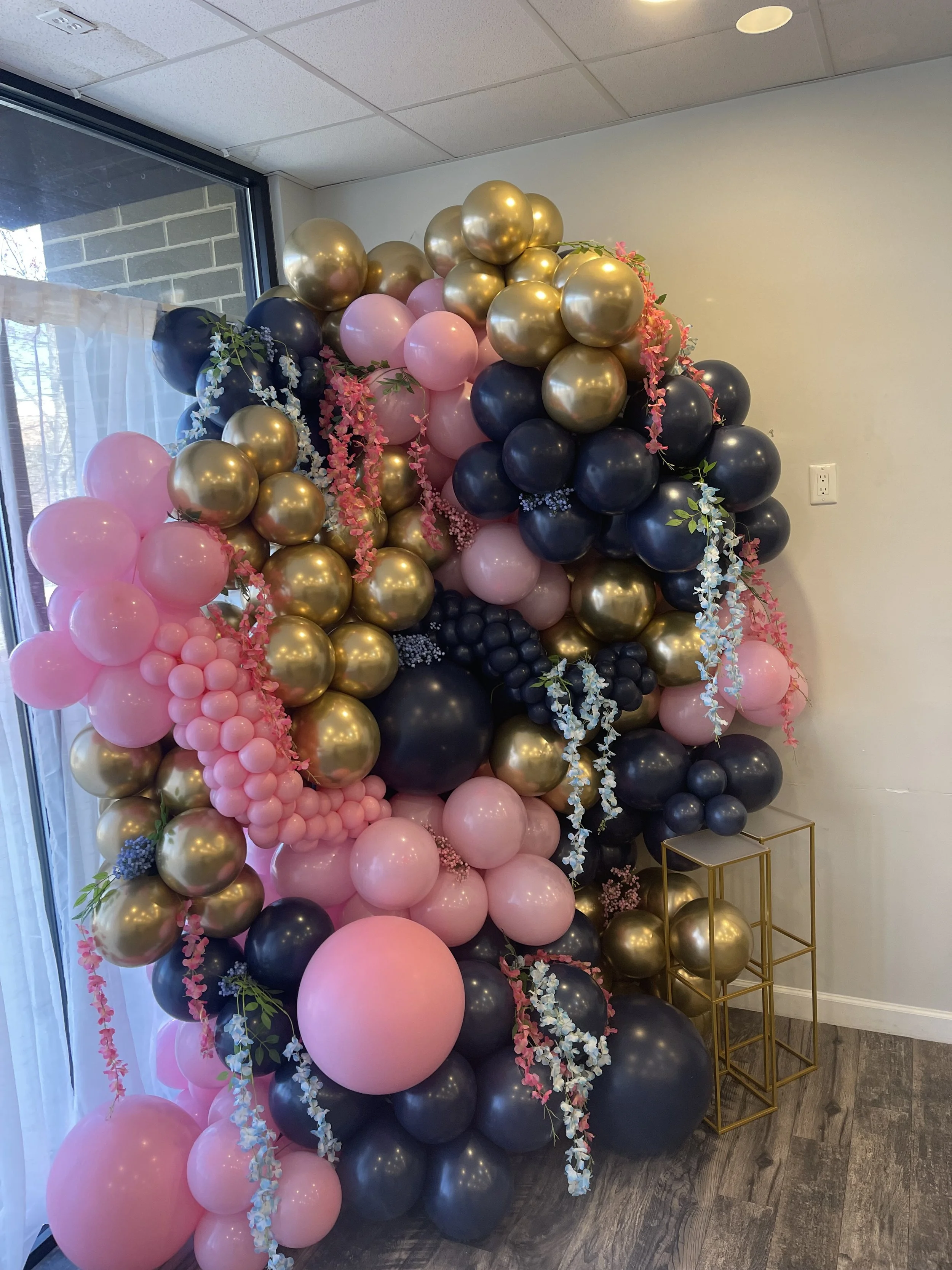 Colorful Balloon Wall featuring gold, pink, and blue balloons, with hanging floral accents.
