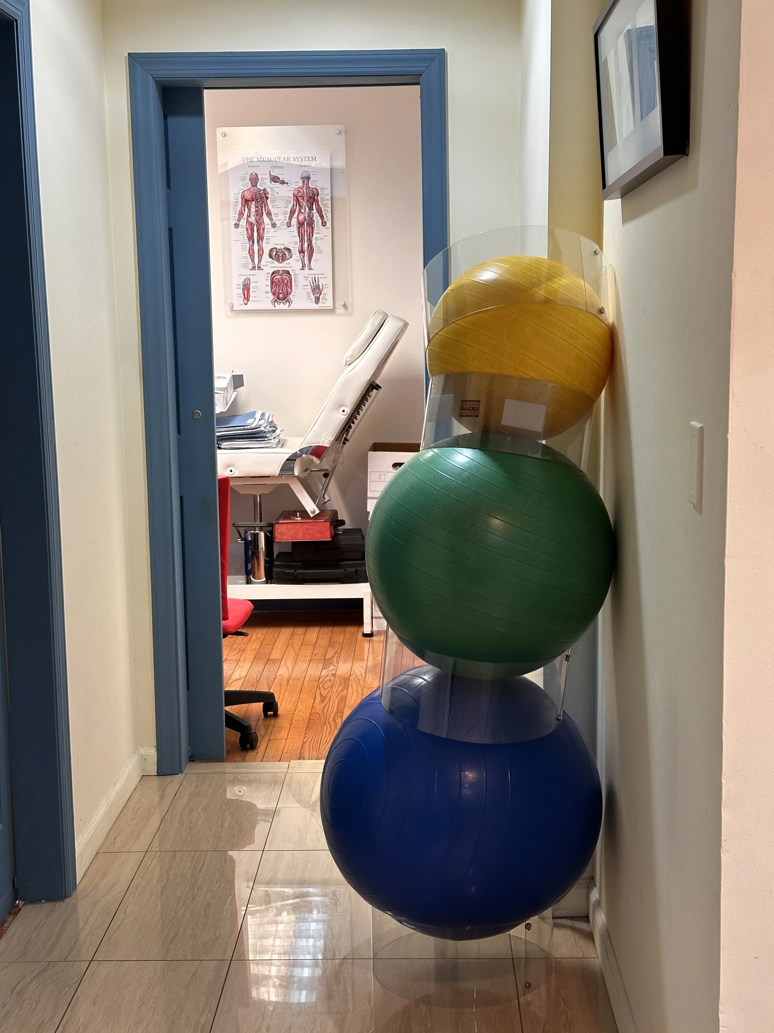 Stacked exercise balls in yellow, green, and blue along a wall in a medical office hallway
