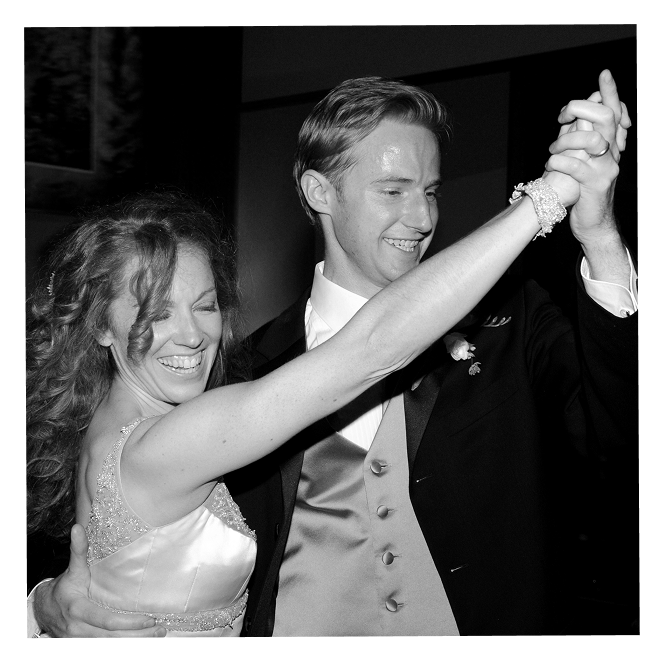 A newlywed couple is happily walking out of a wedding, surrounded by friends throwing confetti. The bride is holding a bouquet and wearing a white wedding dress, while the groom is in a dark suit and tie. They are smiling and seem joyful.