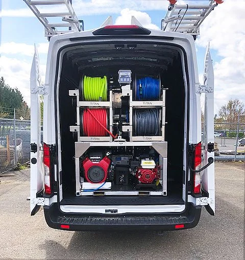 Open van with equipment including high-pressure hoses in green, blue, red, and black, a red hose reel, a red generator, and ladders on top.