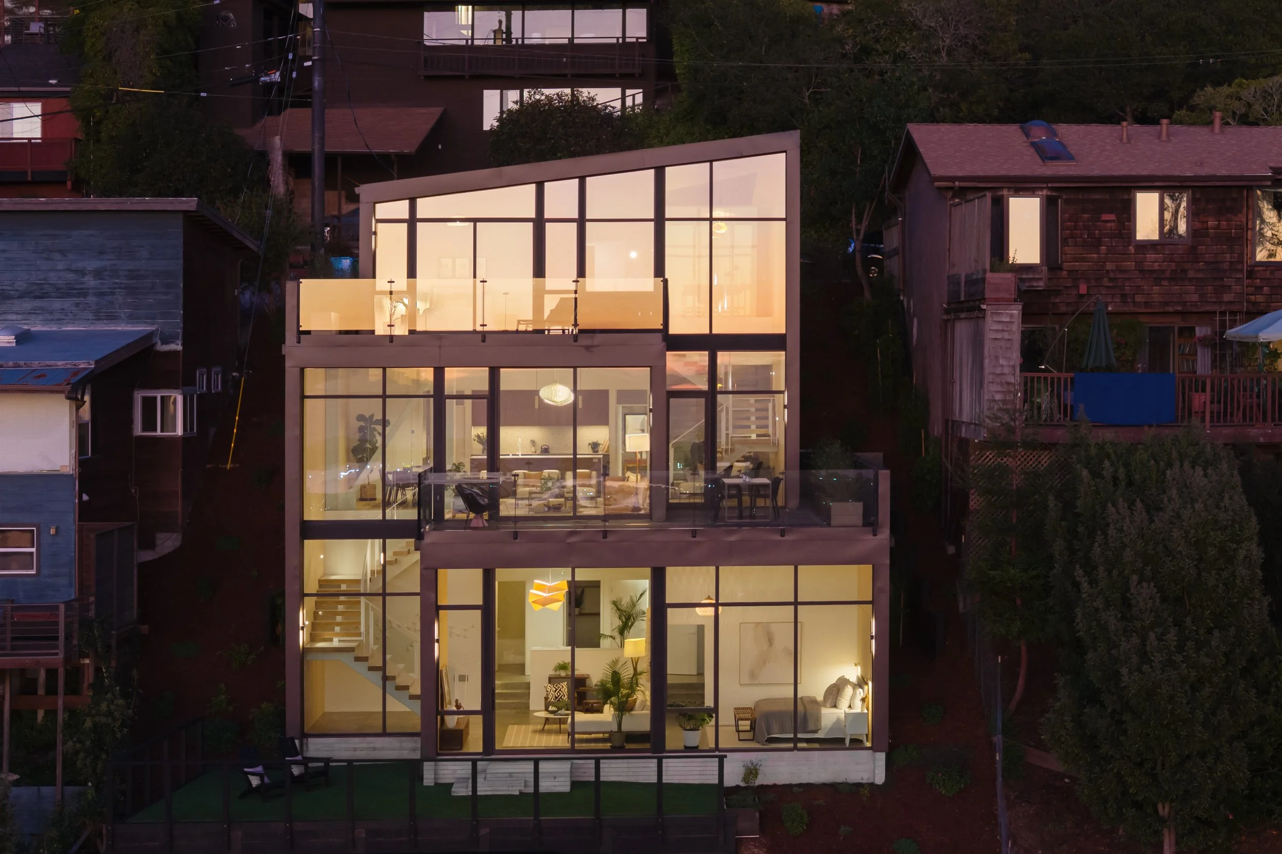 Three-story new construction exterior with dark steel cladding and floor-to-ceiling glazing - View into rooms at dusk - Fold House - Berkeley Hills CA - CB Architecture + Design