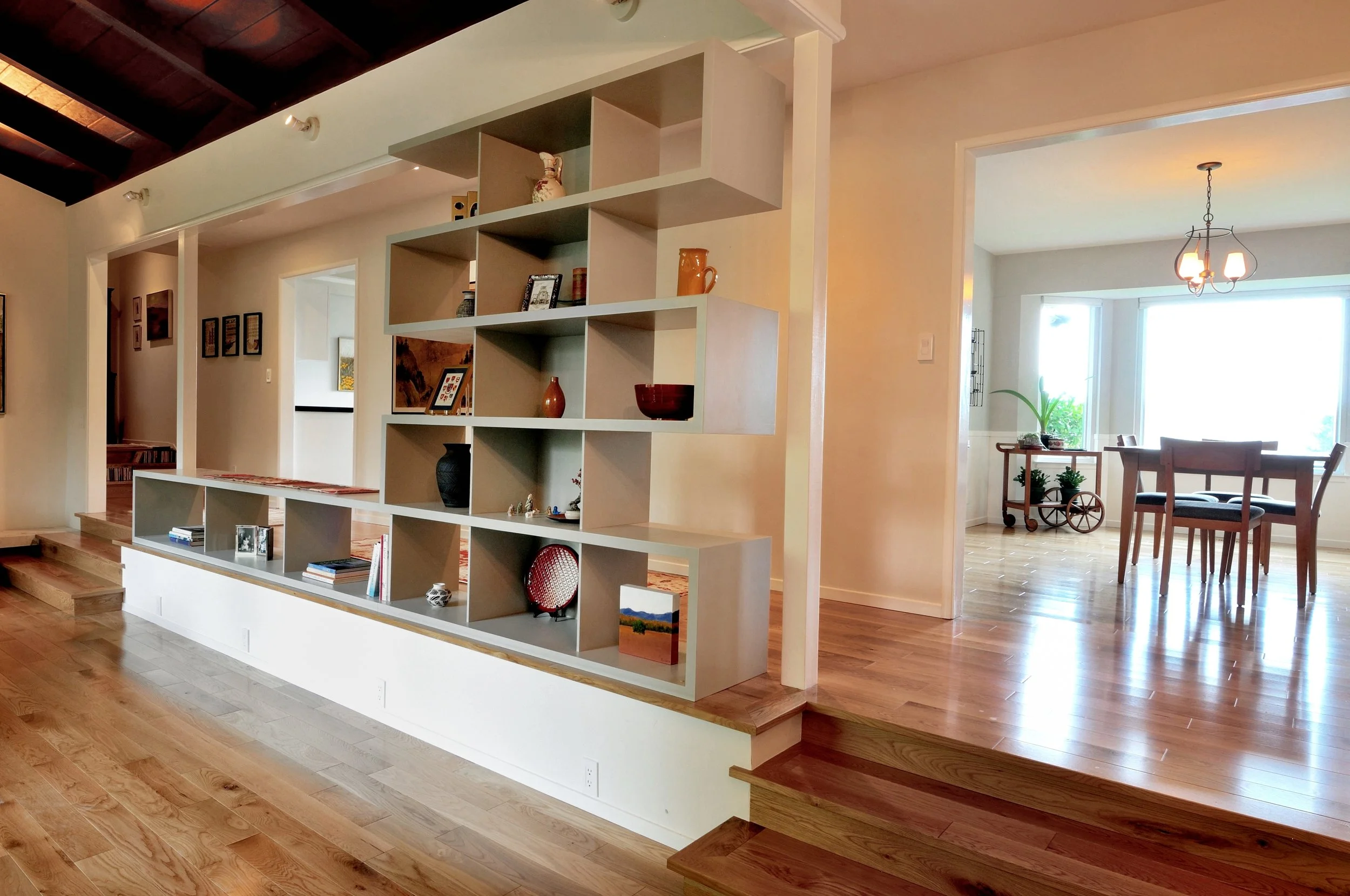 Open concept living space with a decorative shelving unit dividing the area, a dining table with chairs by large windows, and hardwood flooring.